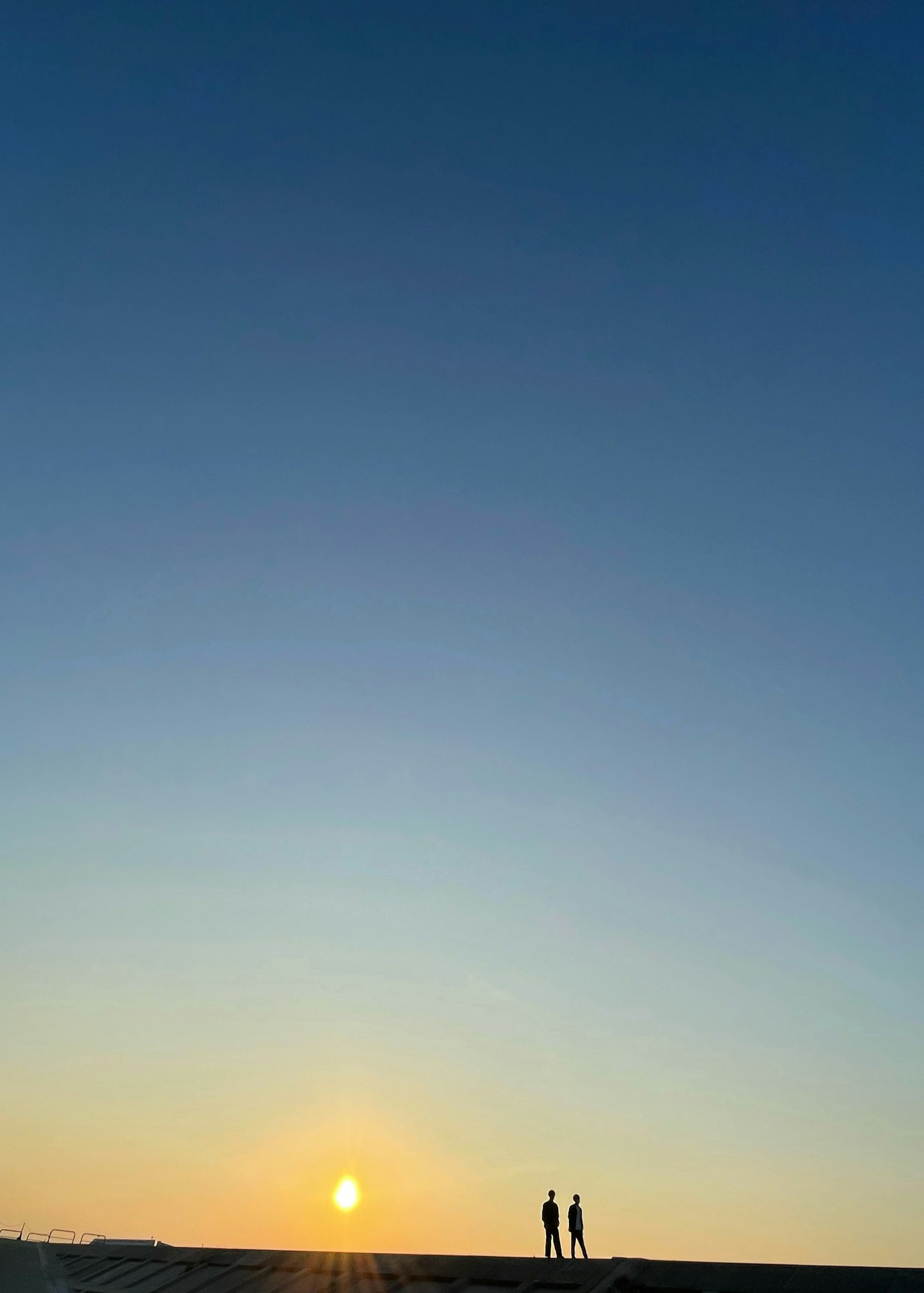 Silhouette von zwei Personen, die gegen einen Sonnenuntergang stehen, weiter Himmel und ruhige Landschaft