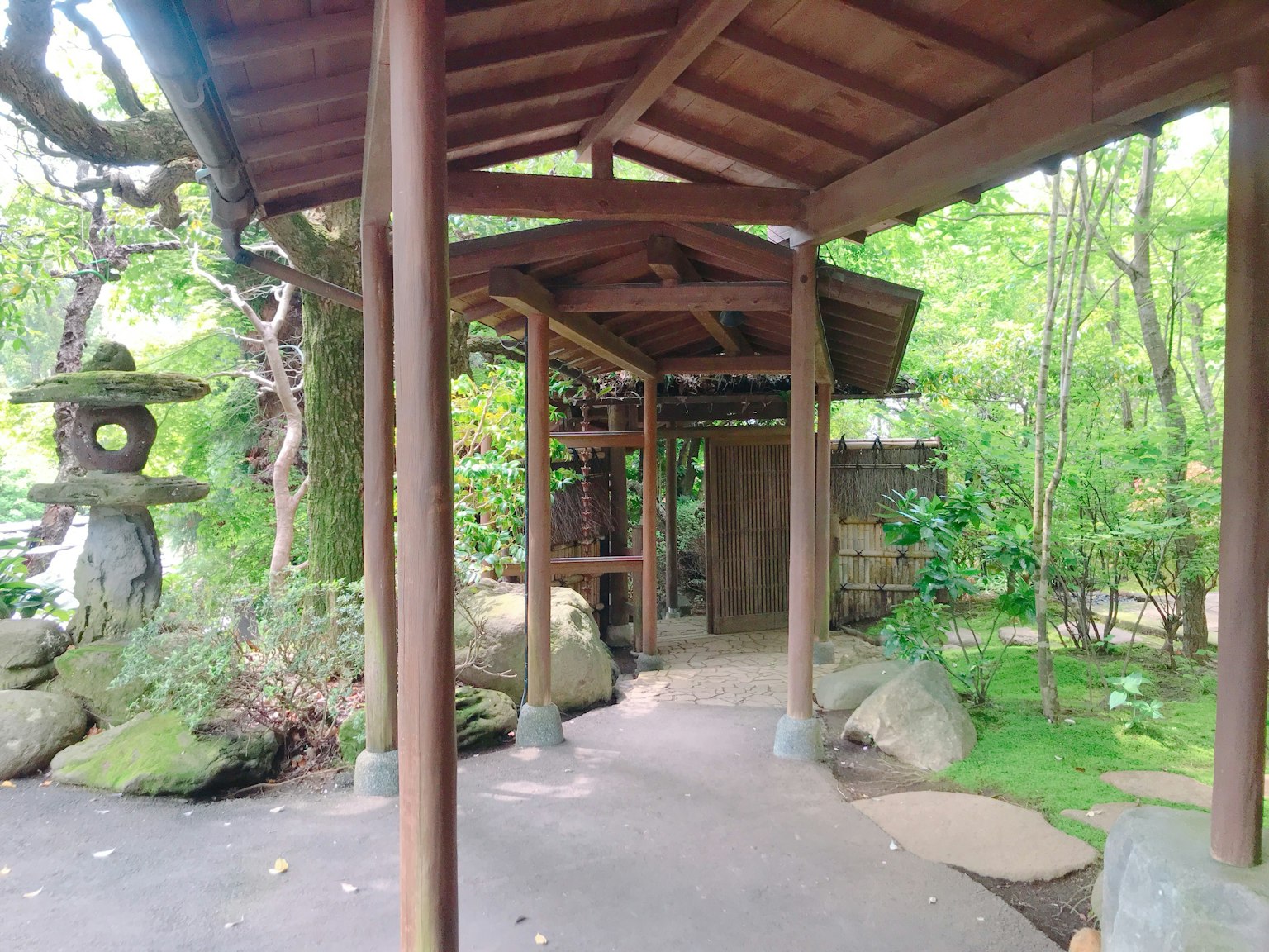 Sendero con techo de madera que conduce a un jardín con linterna de piedra y vegetación exuberante
