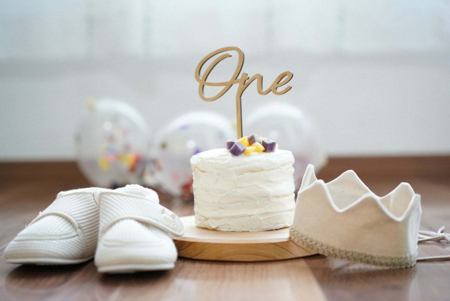 Une décoration d'anniversaire avec des chaussures blanches et un gâteau avec un topper en bois 'Un'