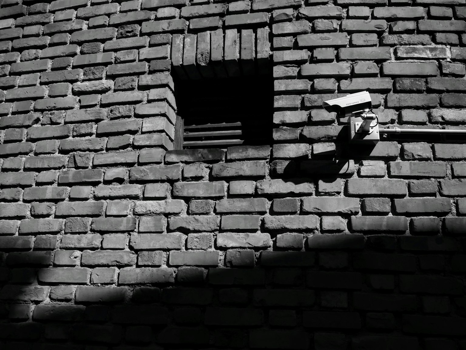 Black and white brick wall featuring a small window and security camera
