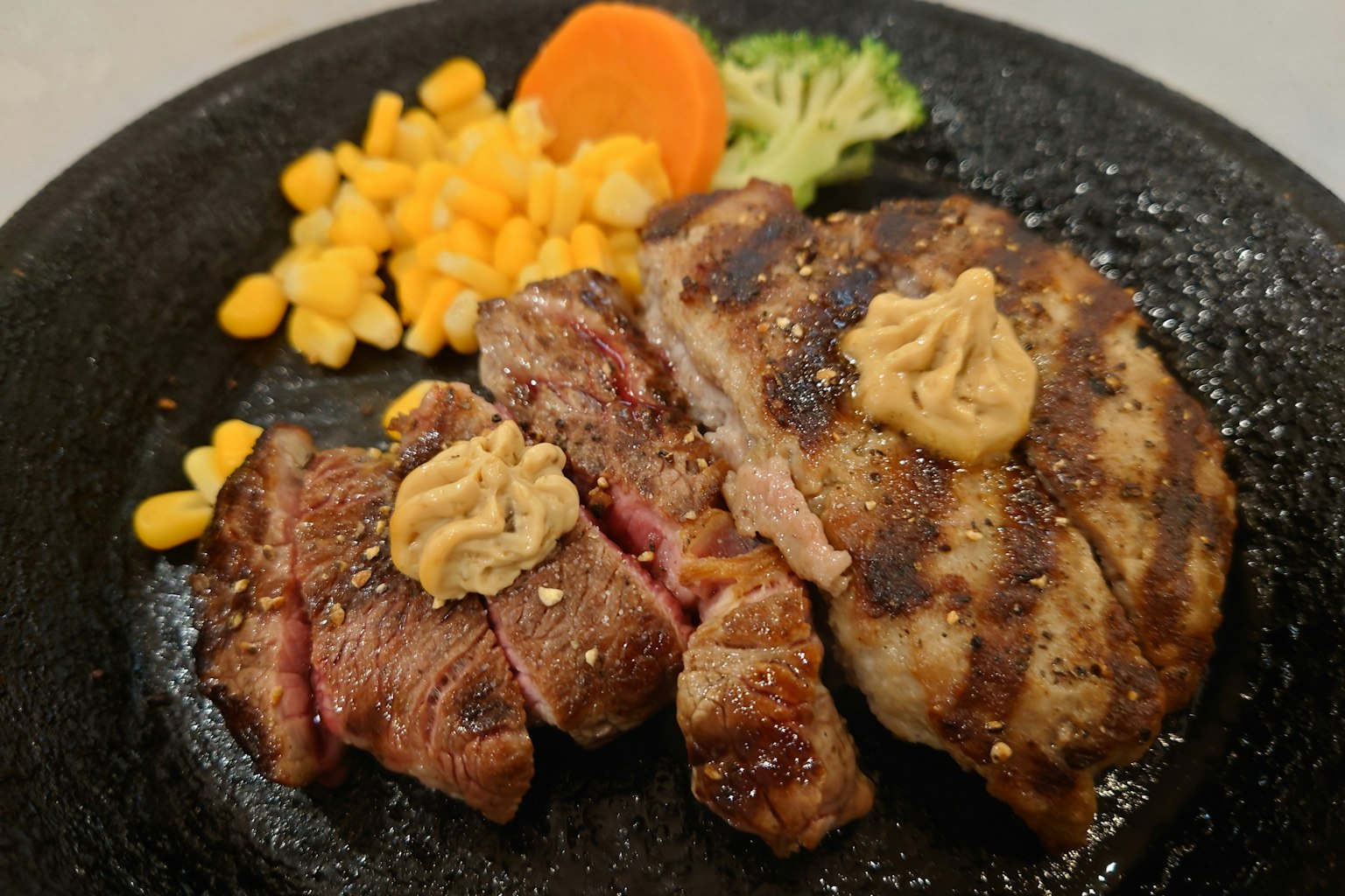 Steak panggang disajikan di piring panas dengan jagung dan wortel sebagai pendamping
