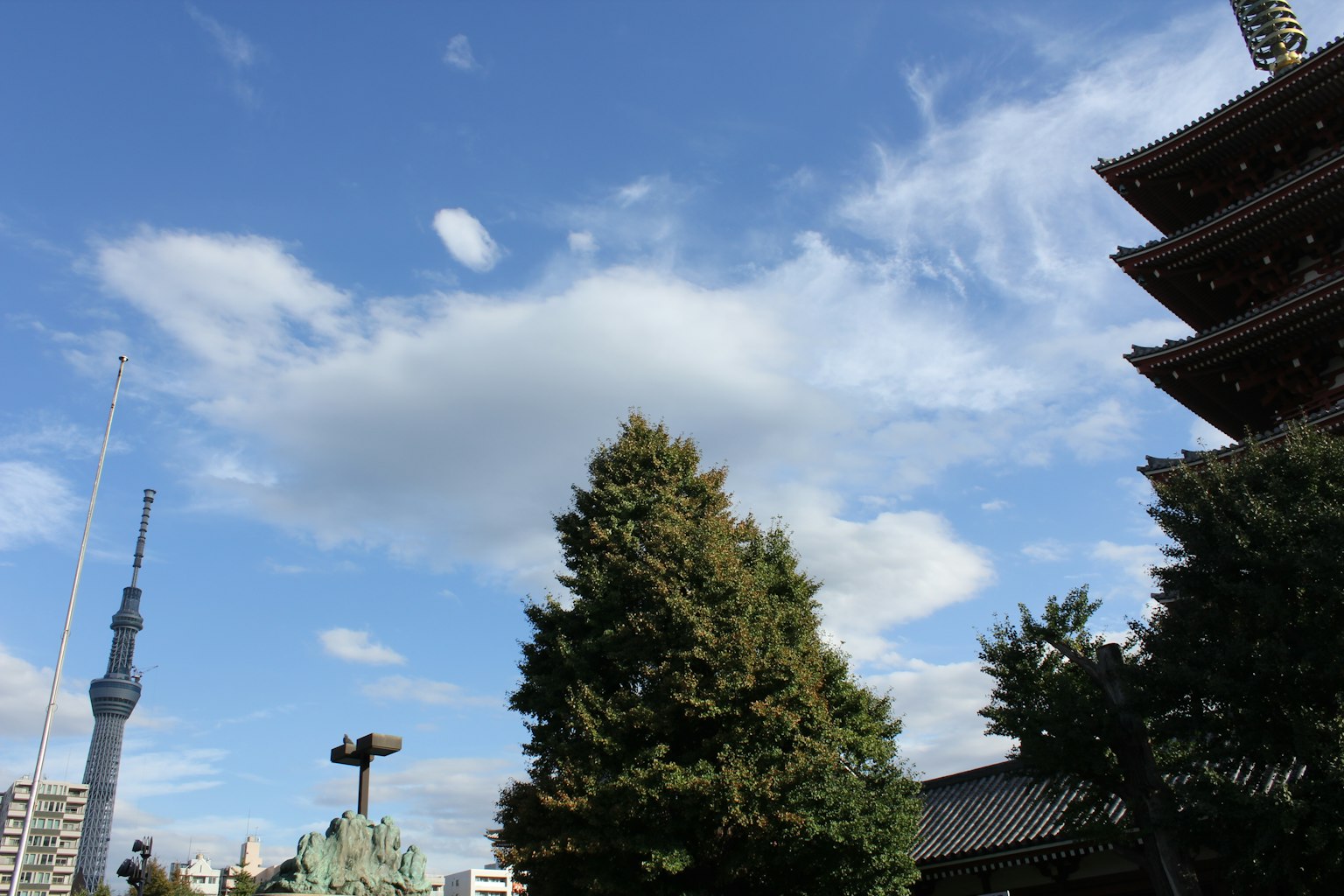 Una vista con una pagoda a cinque piani e un albero alto sotto un cielo blu con la Tokyo Skytree visibile