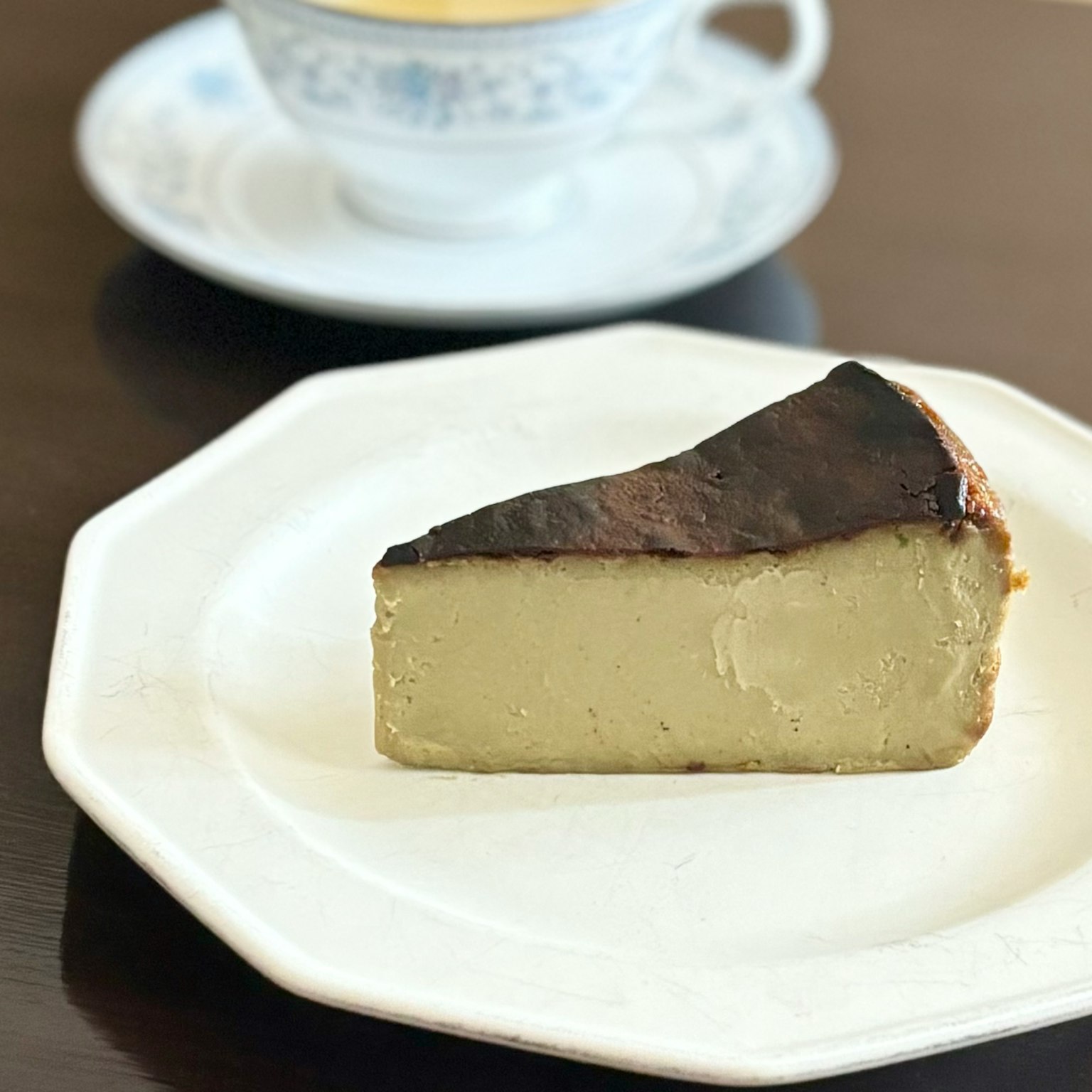 一塊焦燒起司蛋糕放在盤子上，背景有一杯茶