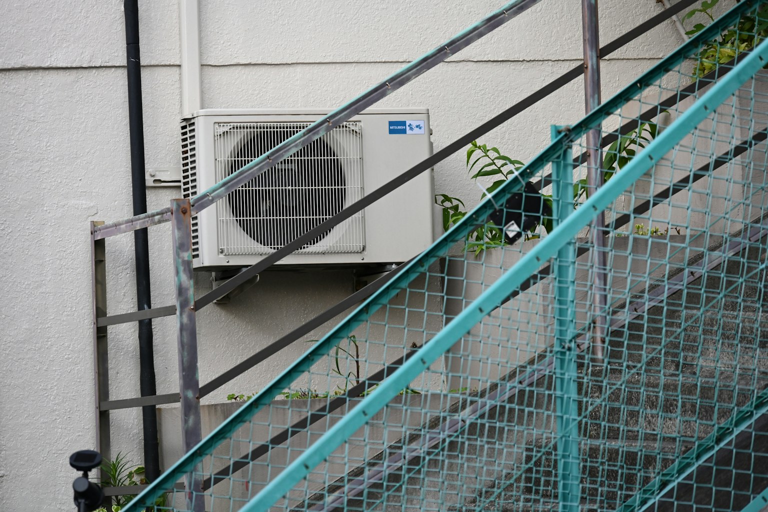 Unidad de aire acondicionado montada en una pared junto a una escalera con valla de malla