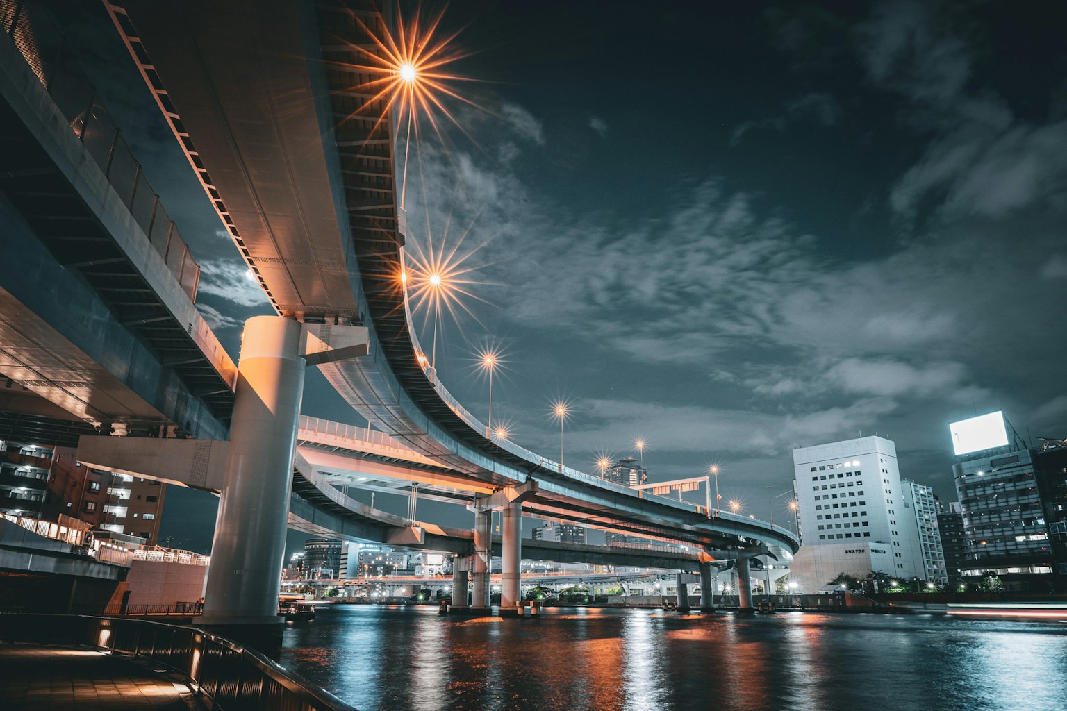 Paisaje urbano nocturno con pasos elevados y reflejos en el agua