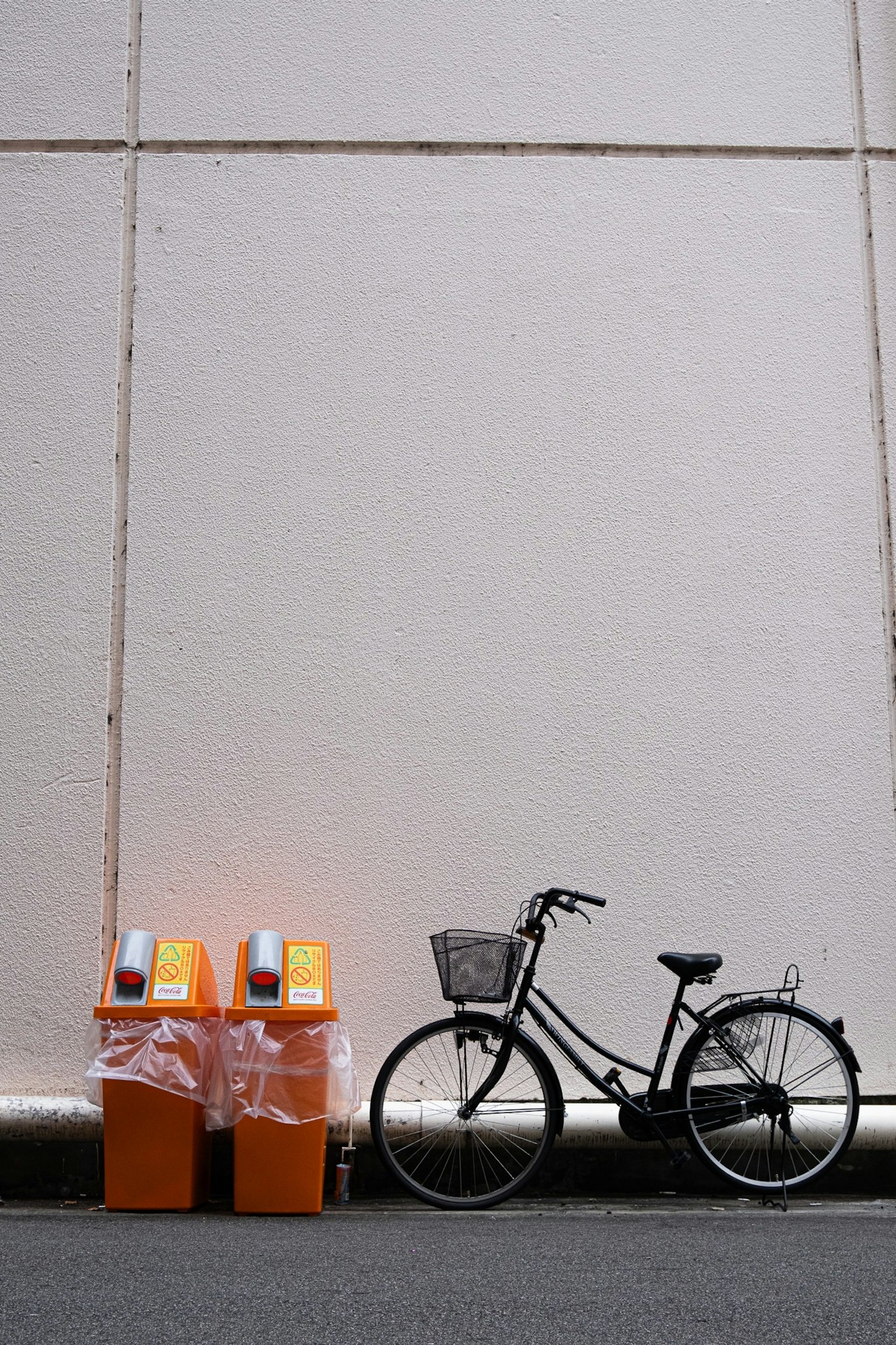 Zwei orangefarbene Mülltonnen und ein schwarzes Fahrrad vor einer weißen Wand