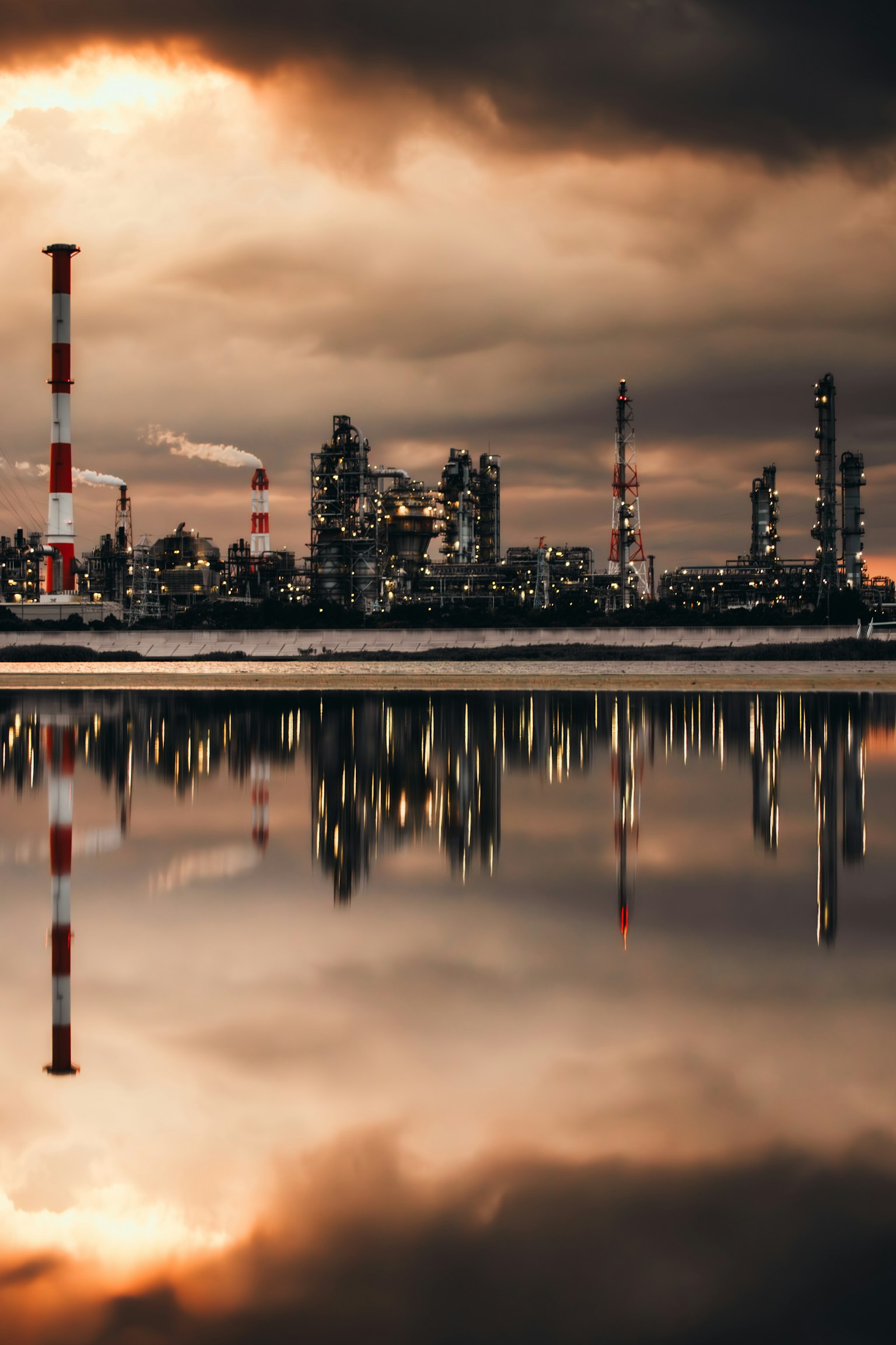 工業地帯の反射がある夕暮れの風景 赤と白の煙突が立ち並ぶ