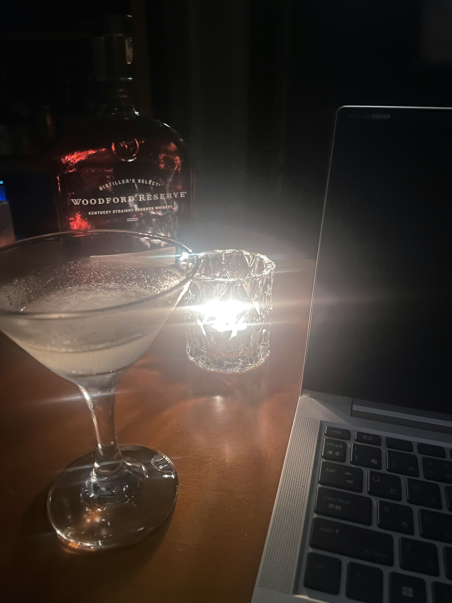 Una scena con un bicchiere di cocktail una candela accesa e un laptop su un tavolo