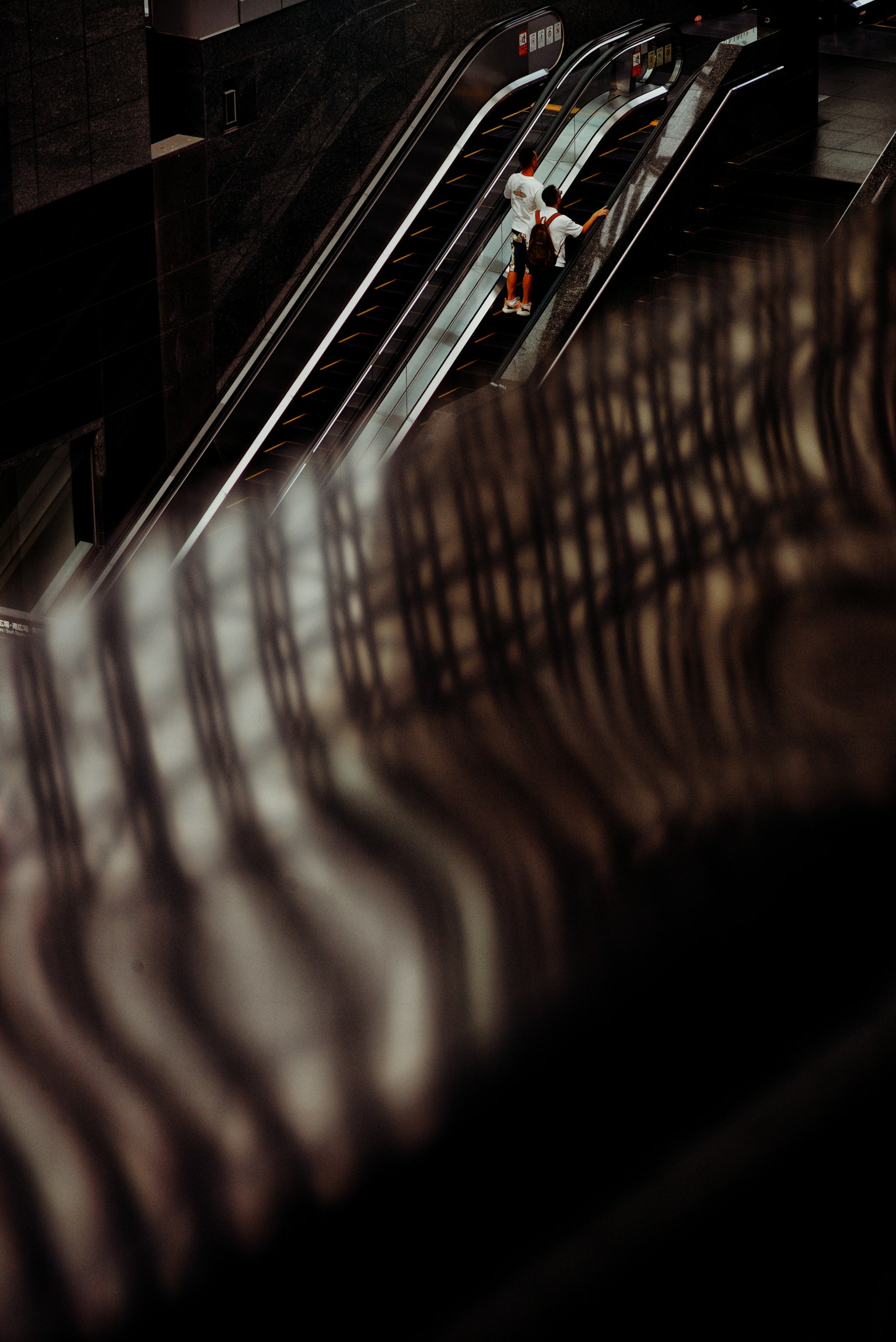 Una persona su una scala mobile con ombre su una ringhiera metallica