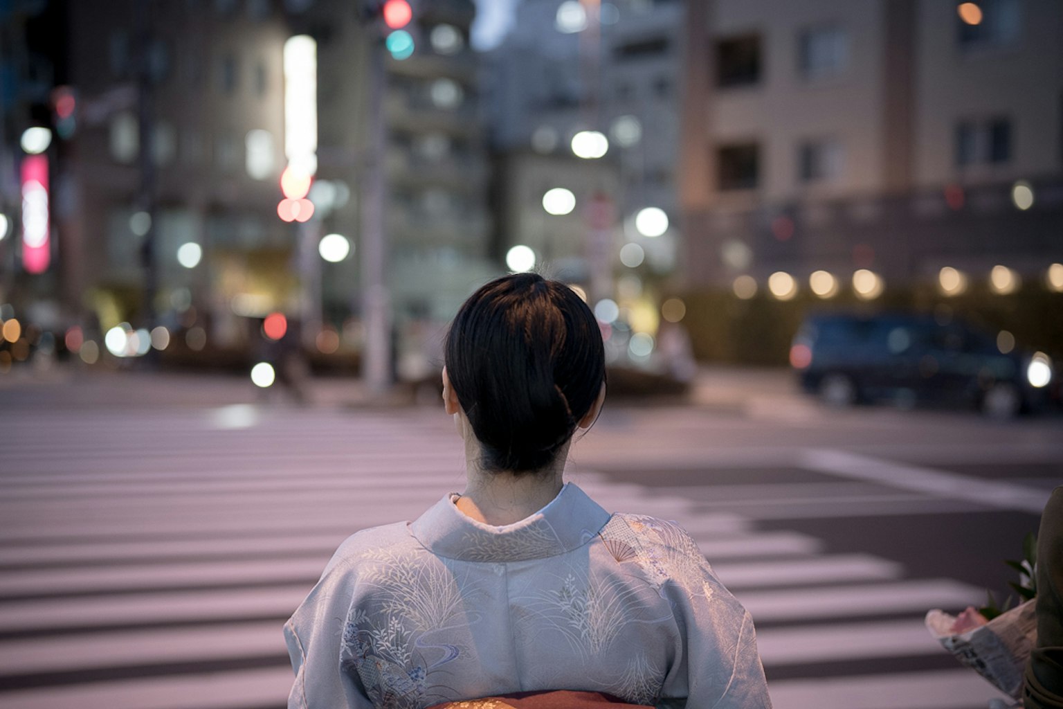 Back view of a woman in traditional attire at a city crosswalk at night
