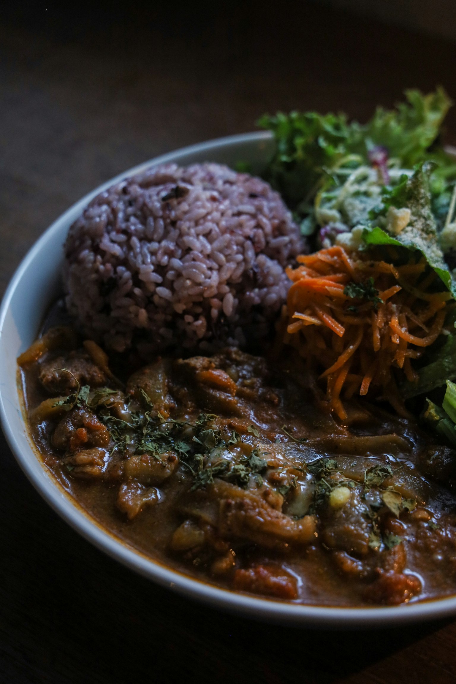 Un plato de guiso con arroz morado y ensalada de verduras