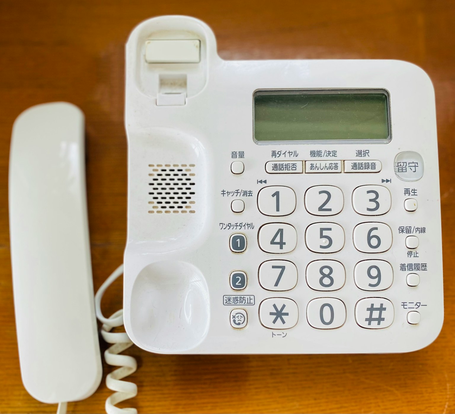 Weißes Festnetztelefon mit Hörer auf einem Holztisch