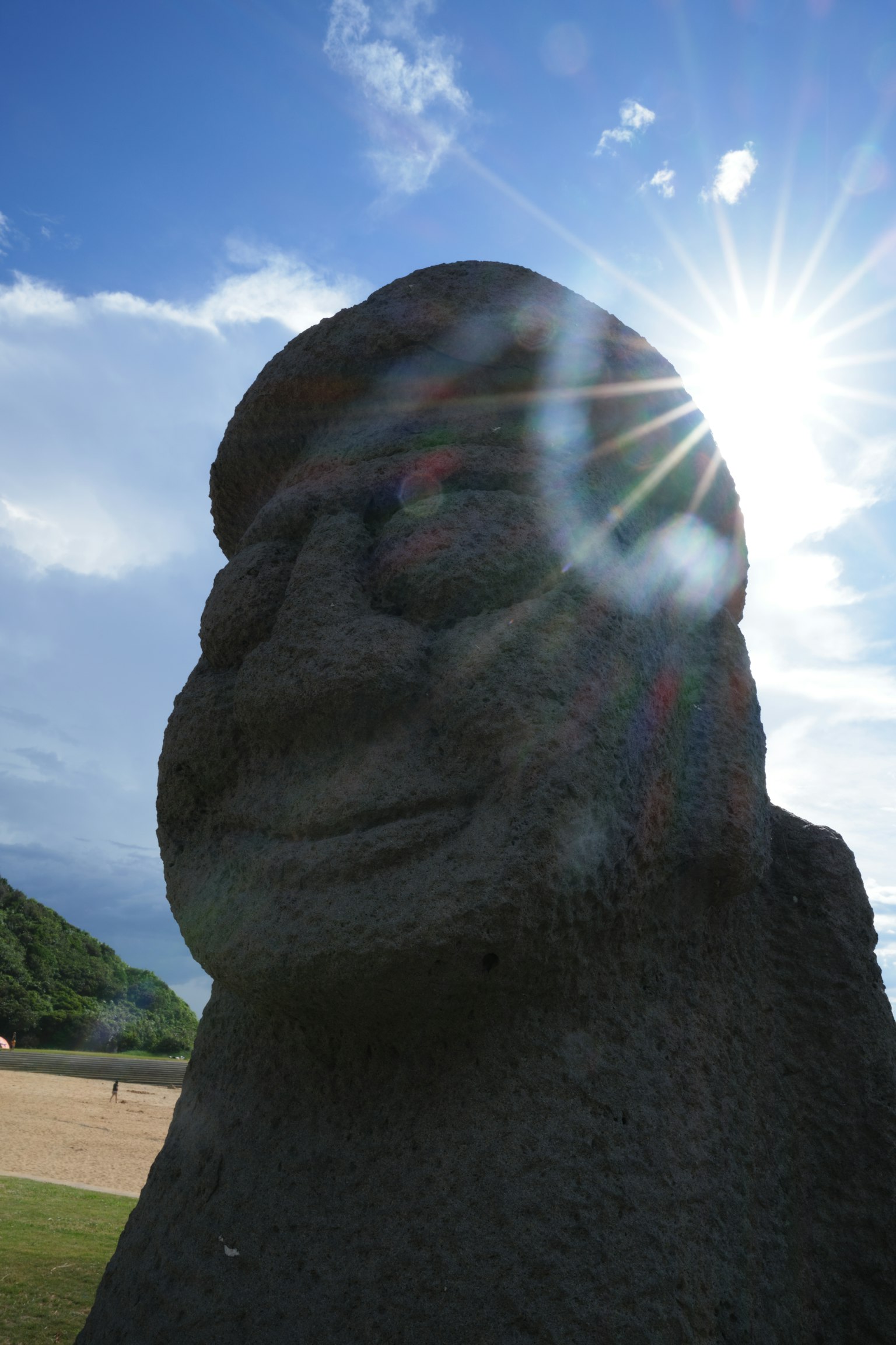Primer plano de una estatua de piedra iluminada por la luz del sol con cielo azul y nubes al fondo
