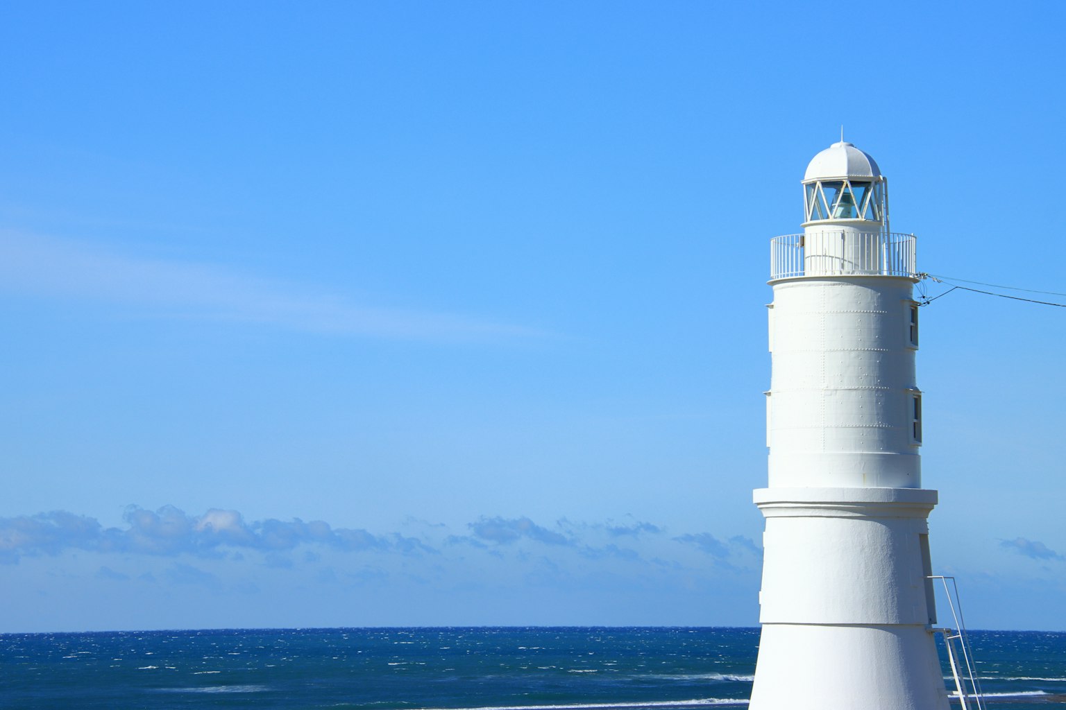Weißer Leuchtturm vor blauem Himmel und Meer