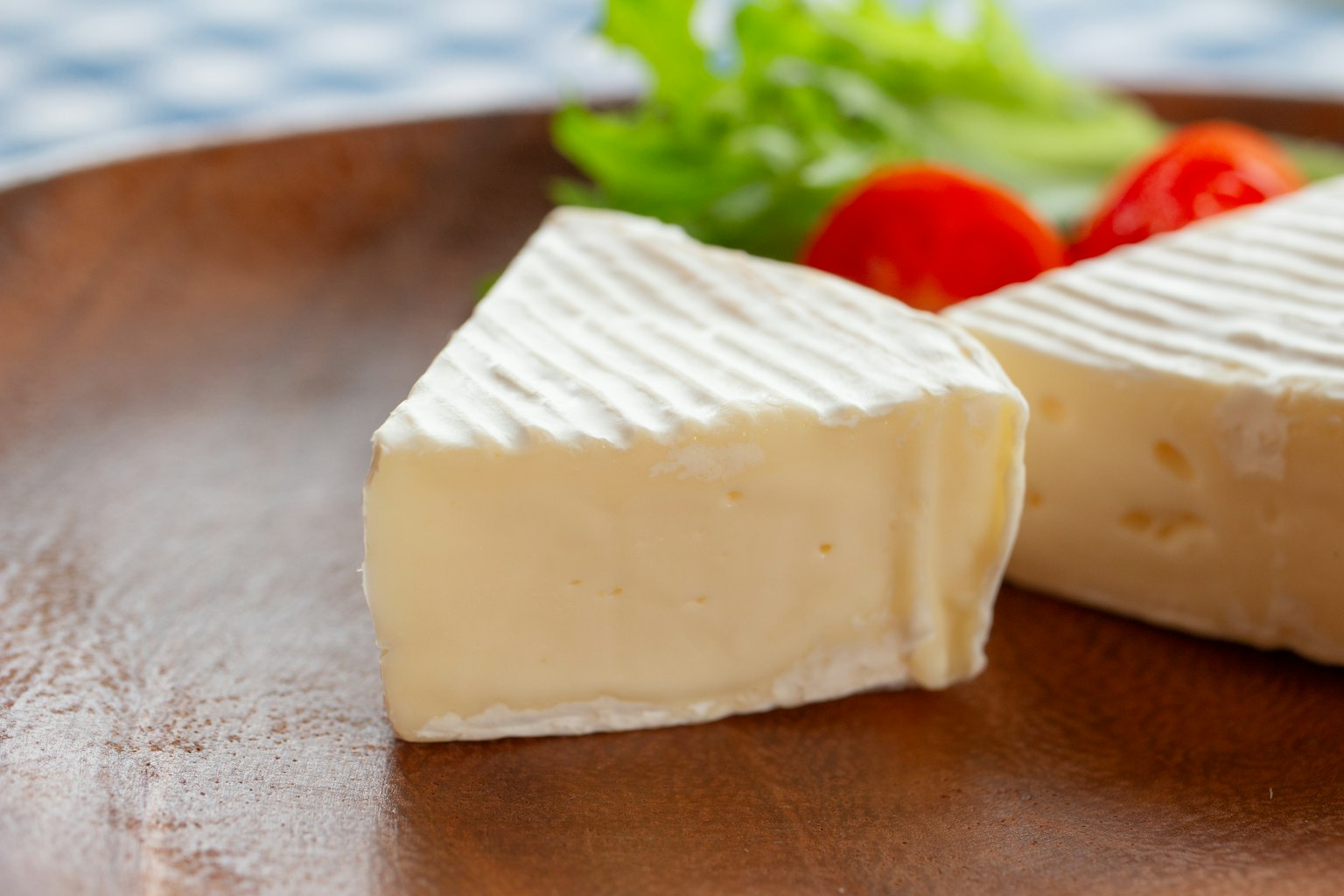 Creamy Brie cheese slice with fresh tomatoes and lettuce on a wooden plate