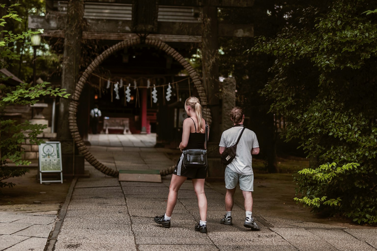 Zwei Touristen stehen vor einem Torii eines Schreins in einer üppigen grünen Umgebung