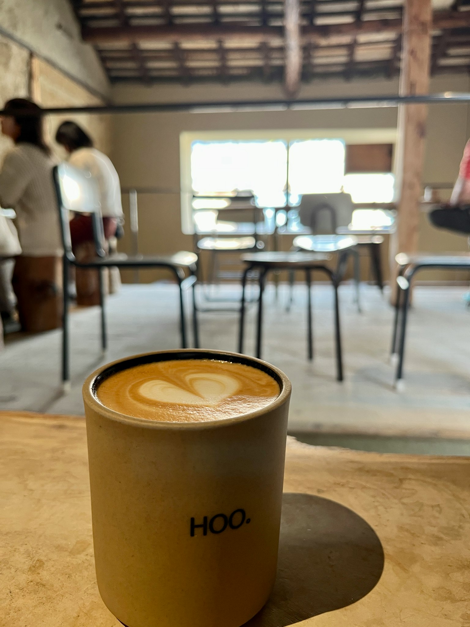 Kaffee mit Latte-Art auf einem Tisch in einem Café mit Menschen im Hintergrund