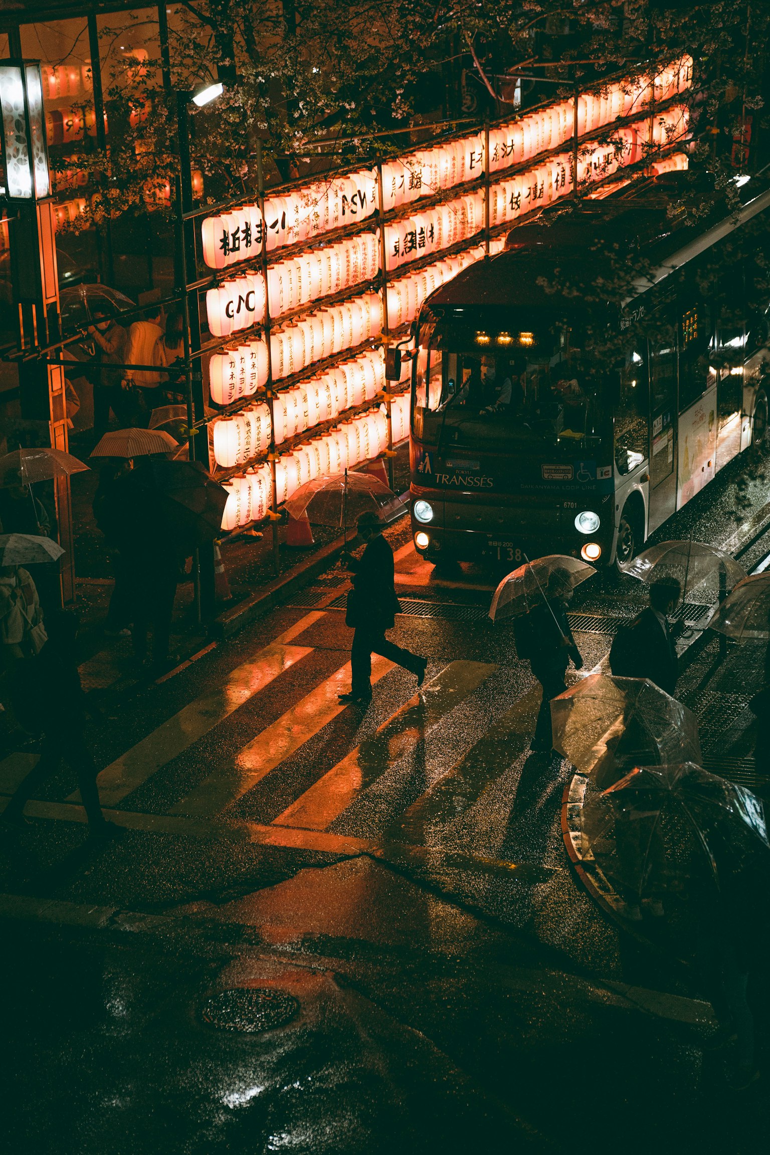 雨の中の交差点で歩く人々とバスの光が映る夜の街