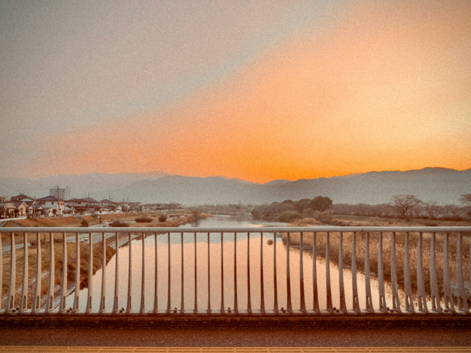 Pemandangan sungai saat matahari terbenam dengan pagar jembatan di latar depan