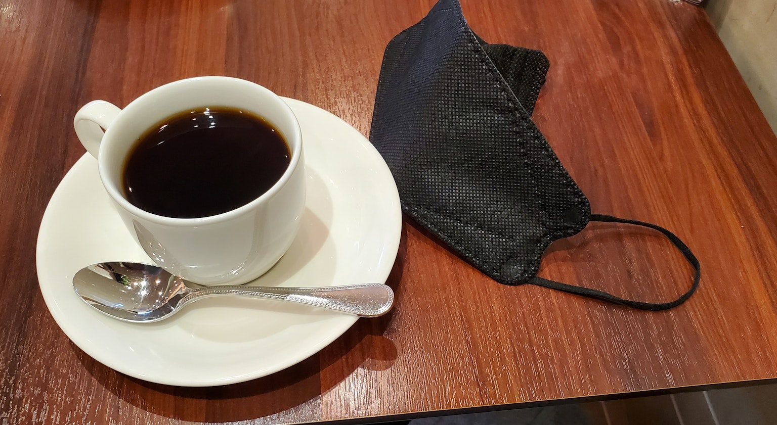 Una taza de café negro y una mascarilla sobre una mesa de madera