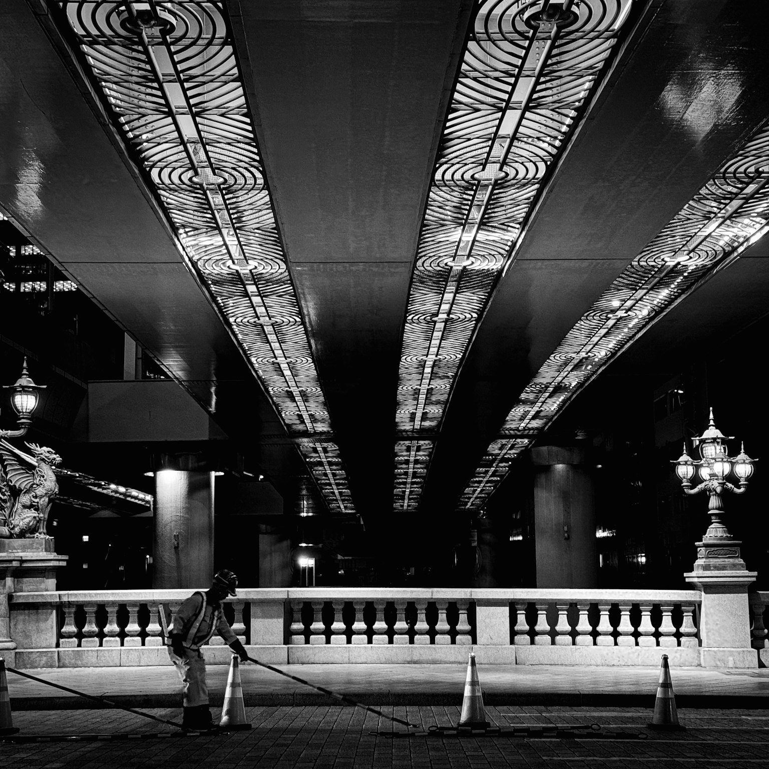 Escena urbana en blanco y negro con una persona trabajando bajo un techo iluminado