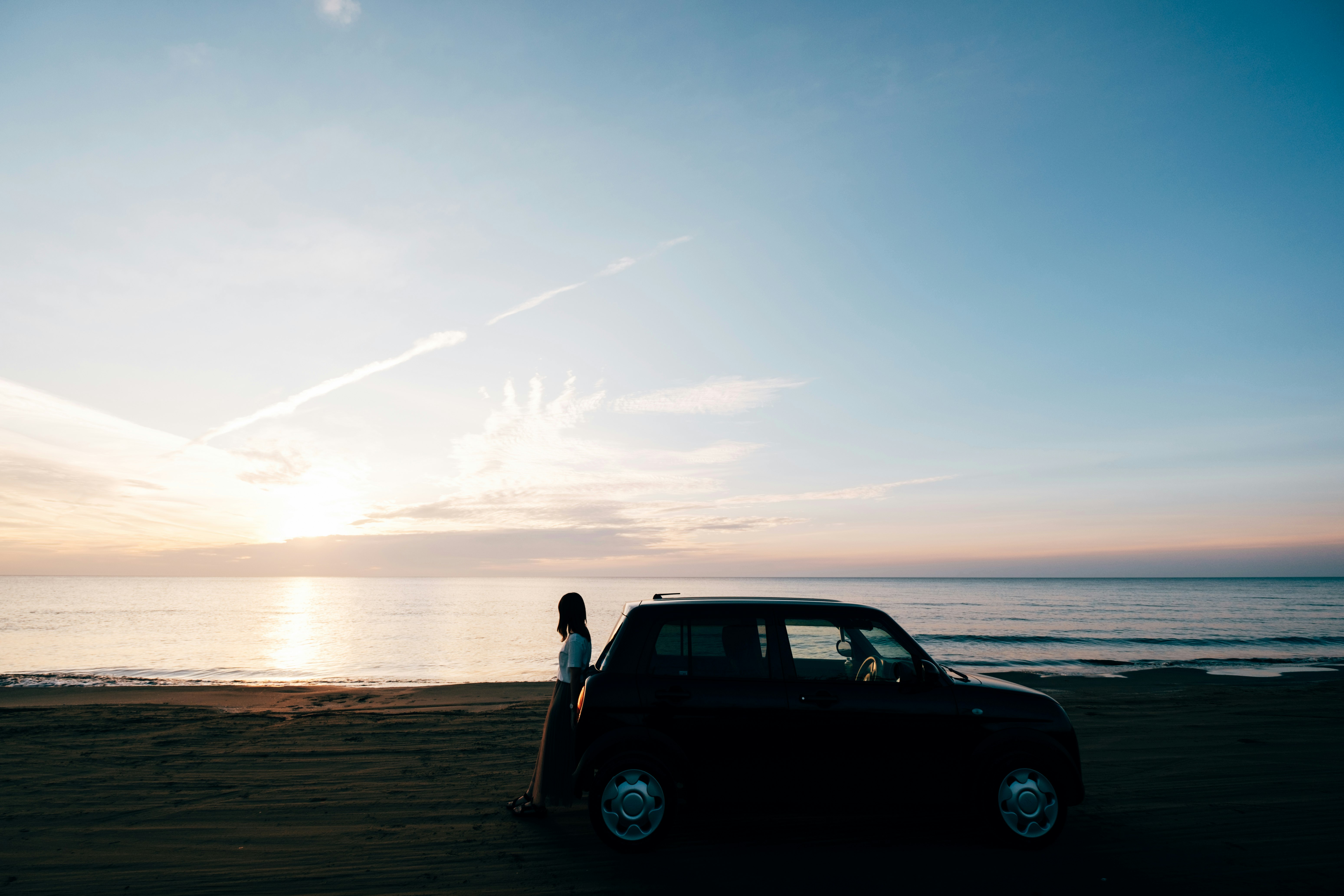 海辺の砂浜に停まる車と夕焼け空の風景