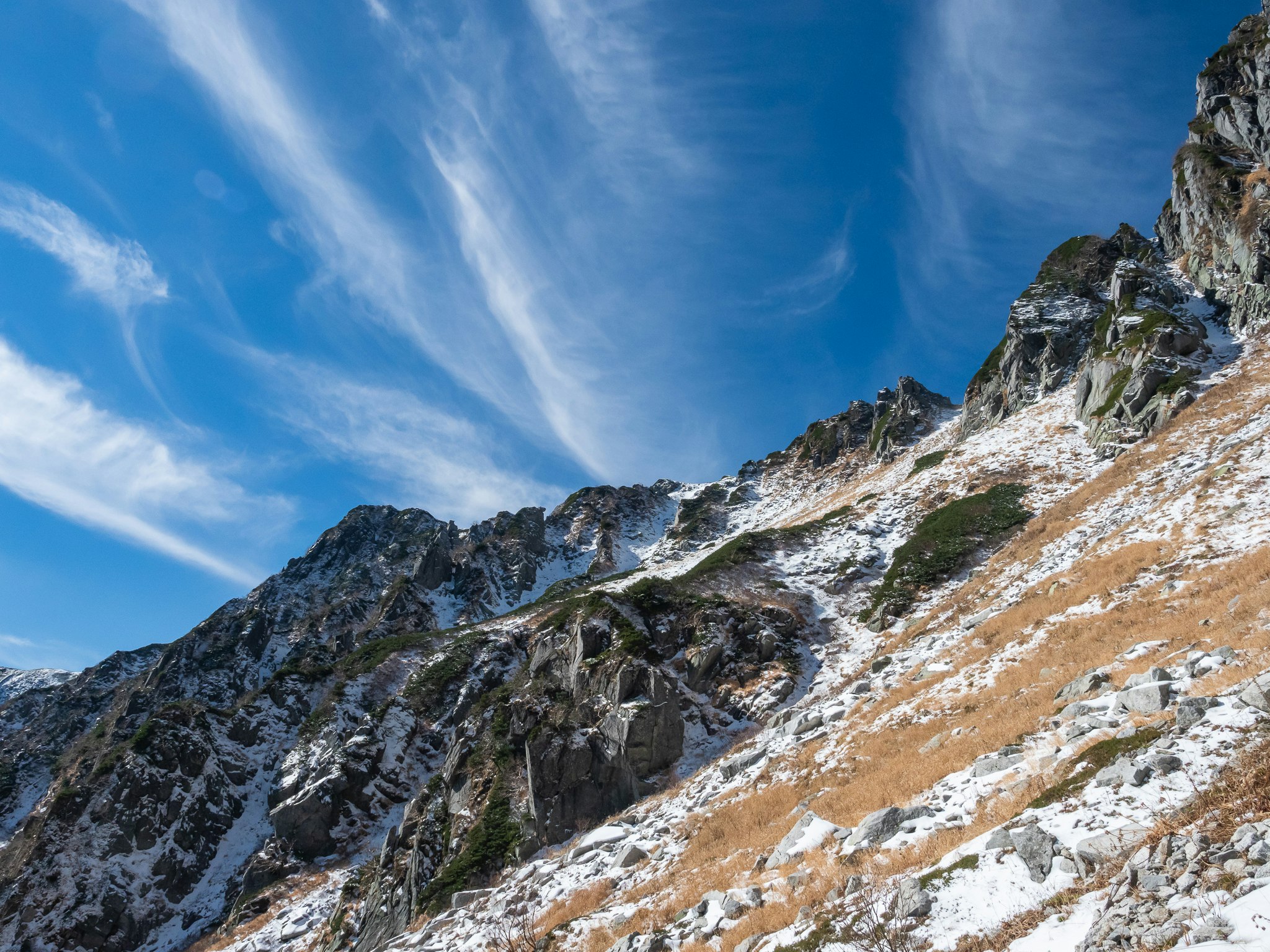 verschneite Berghänge und felsige Gipfel unter blauem Himmel