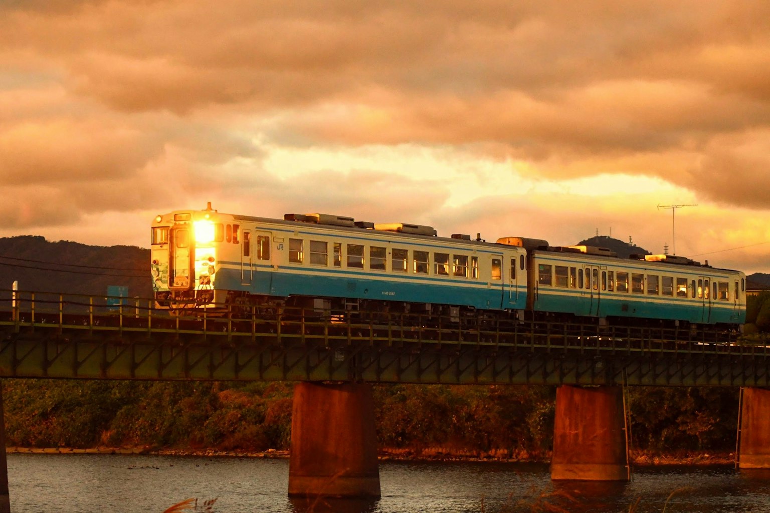 Ein blauer Zug überquert eine Brücke bei Sonnenuntergang