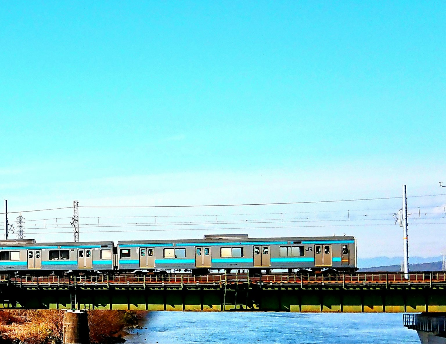 Un treno blu che attraversa un ponte sotto un cielo blu chiaro