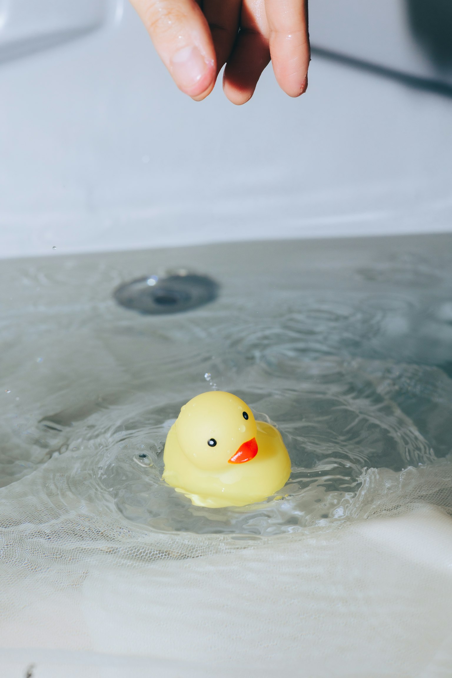 Un pato de goma amarillo flotando en el agua con una mano arriba