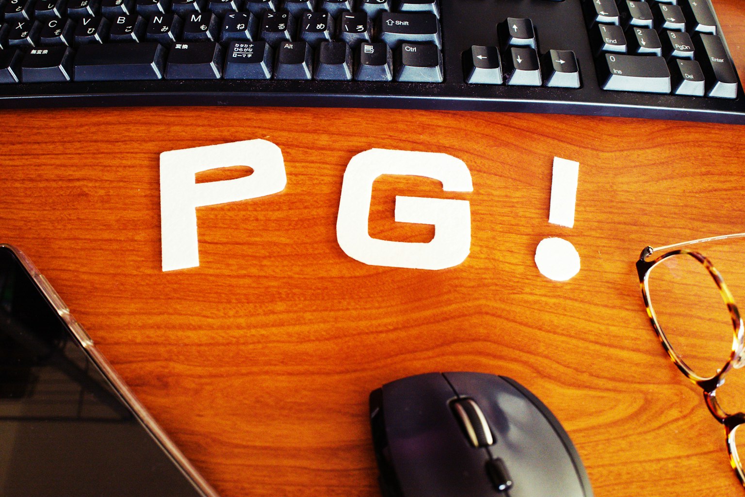 Chữ trắng 'PG!' trên bàn gỗ gần bàn phím và chuột