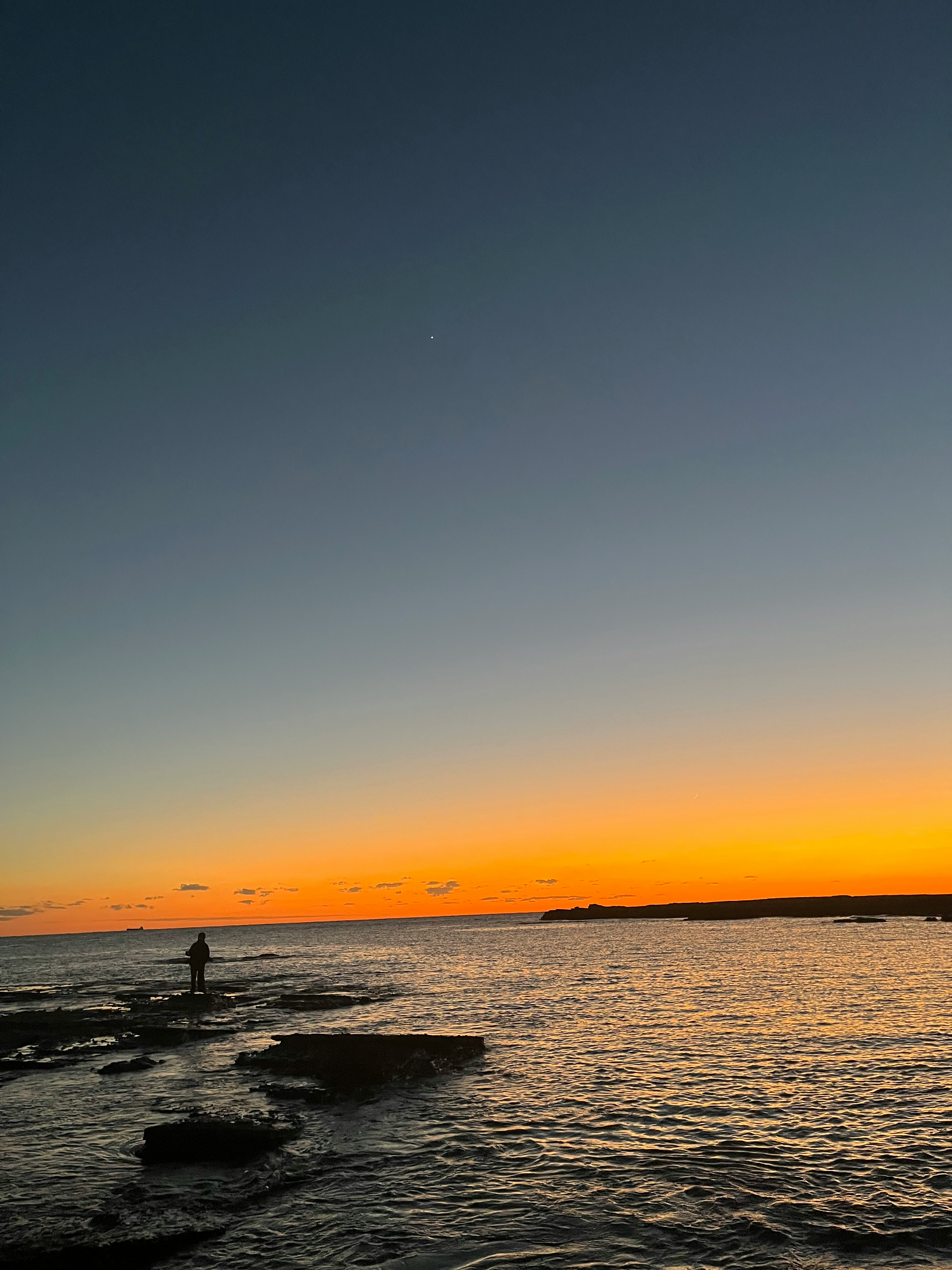 夕焼けの海辺で波打ち際を歩く人