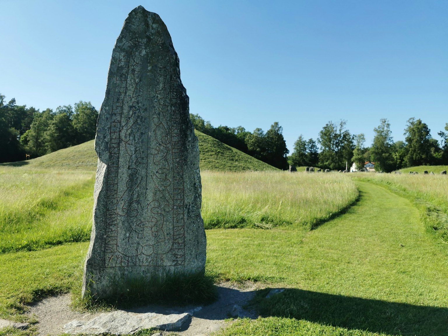 Tall stone monument in a green meadow with a hill in the background