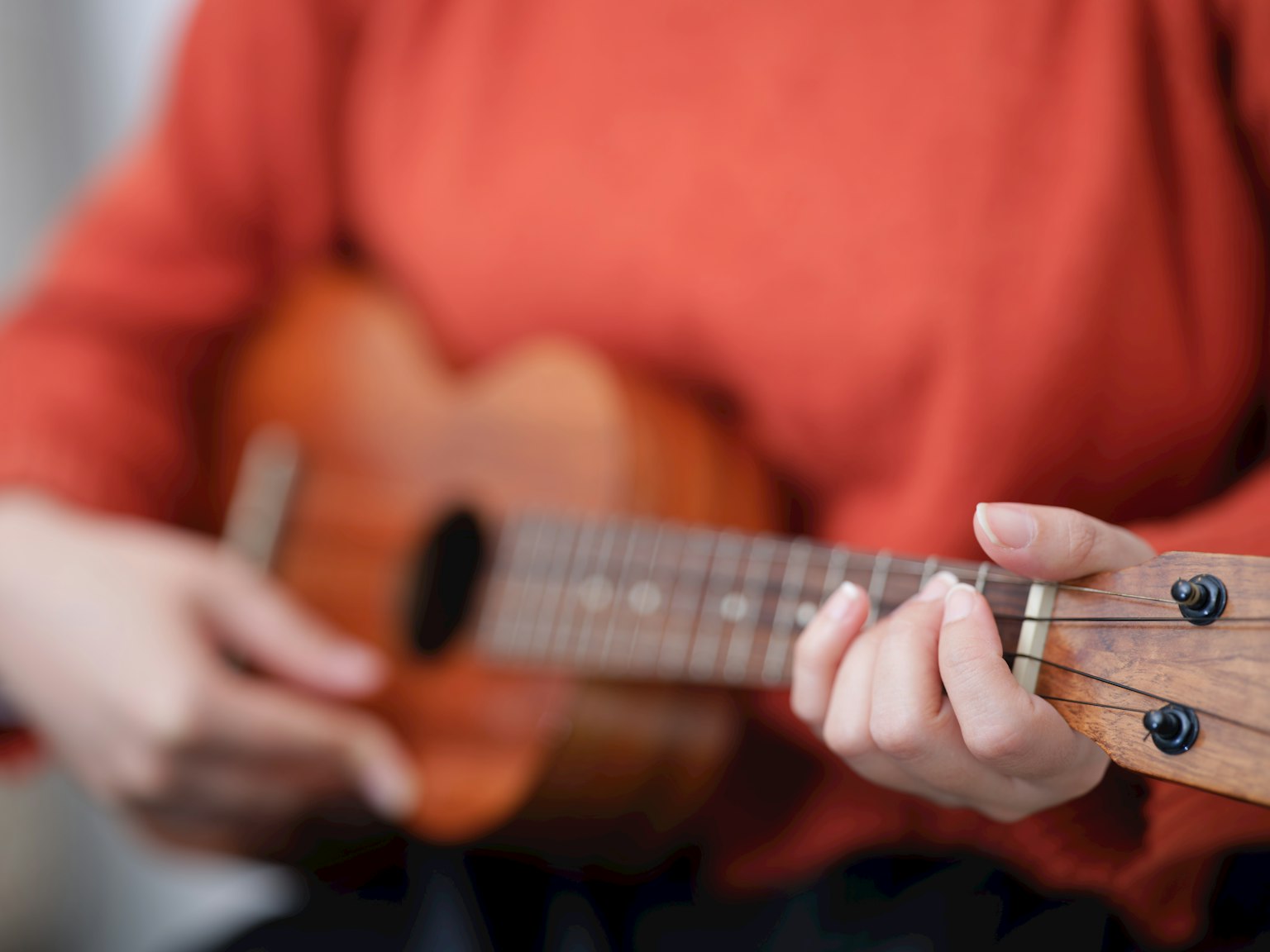 Seseorang yang mengenakan sweater merah sedang bermain ukulele