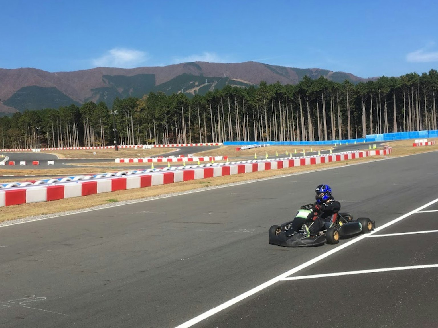 Carrera de karts en un circuito con cielo azul y montañas al fondo