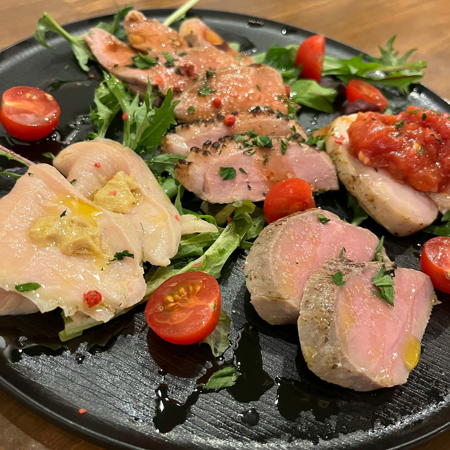 จานดำที่มีจานไก่หลากหลายชนิดประดับด้วยสมุนไพรและมะเขือเทศเชอร์รี่