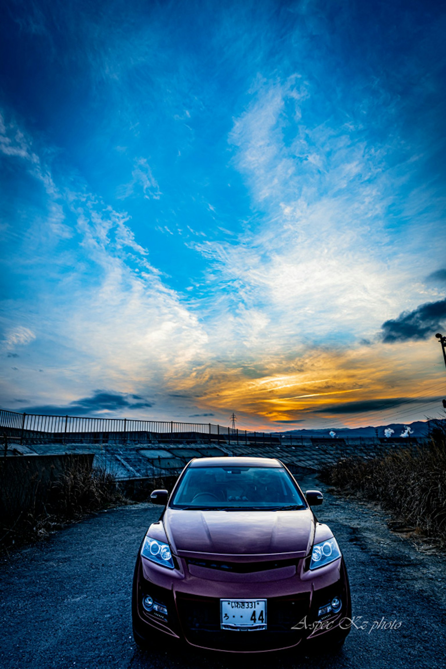 A red car in the foreground with a vibrant sunset and expansive sky