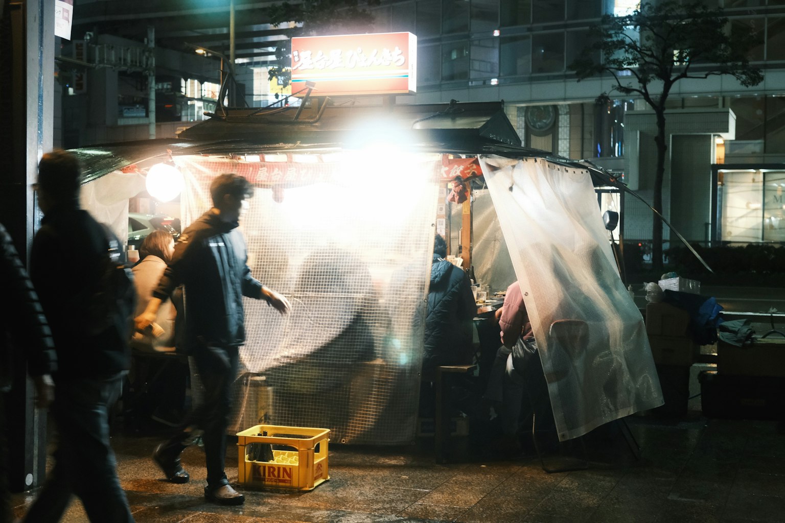夜间场景，人们聚集在一个被透明塑料围住的食品摊位 周围反射的亮光