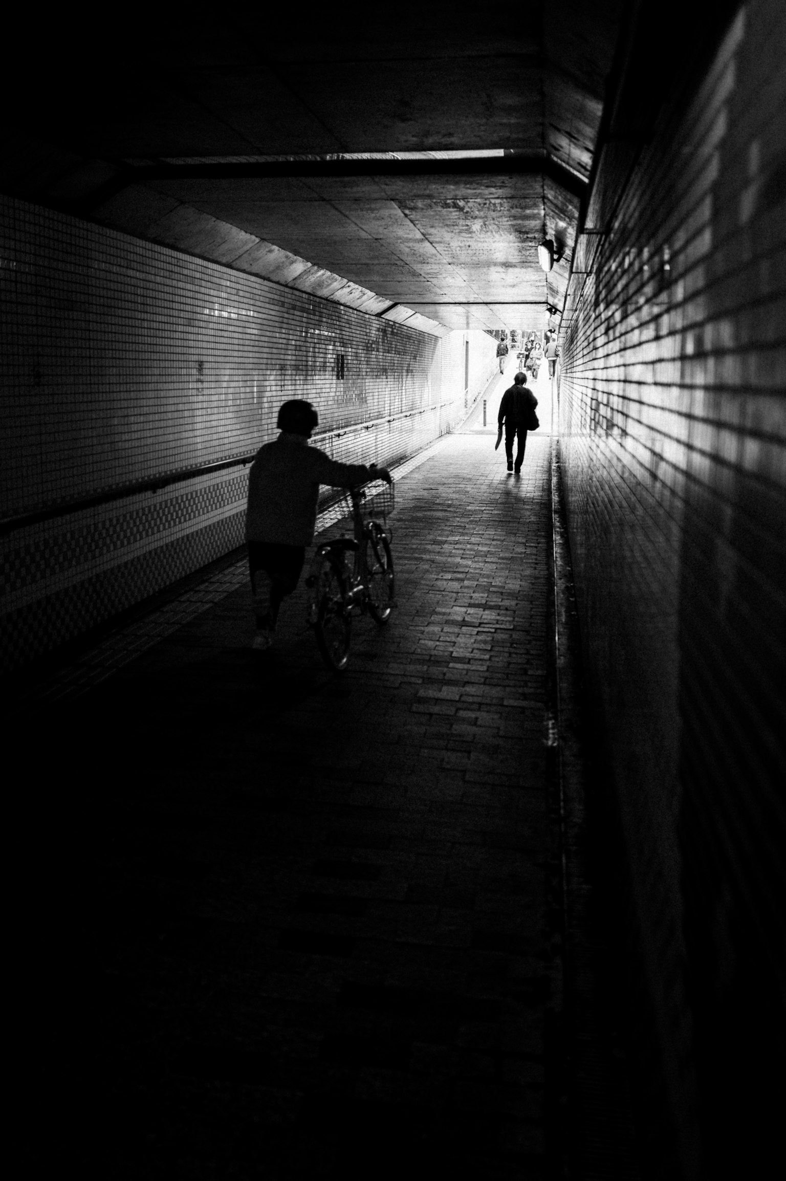 Bambino che spinge una bicicletta in un tunnel buio con una figura che cammina verso la luce