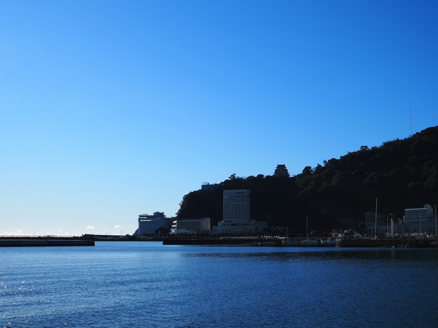 Vista di edifici e colline contro un cielo blu chiaro e un mare calmo
