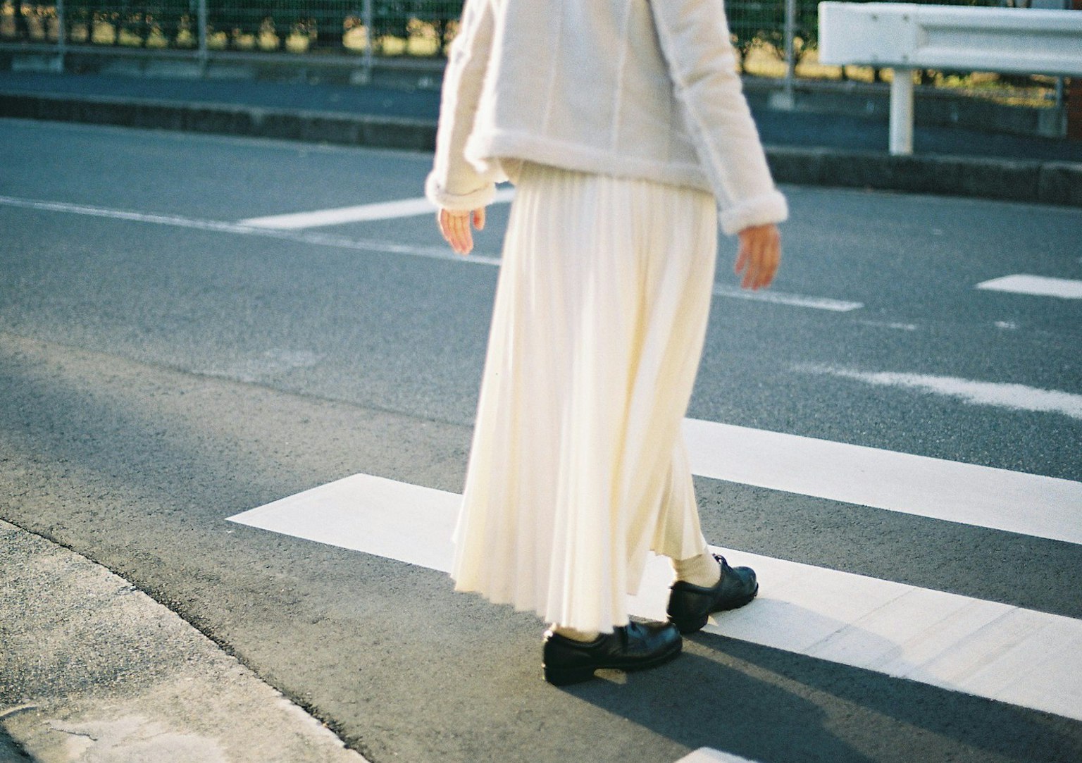 ผู้หญิงใส่กระโปรงพลีทสีขาวเดินอยู่บนทางข้าม