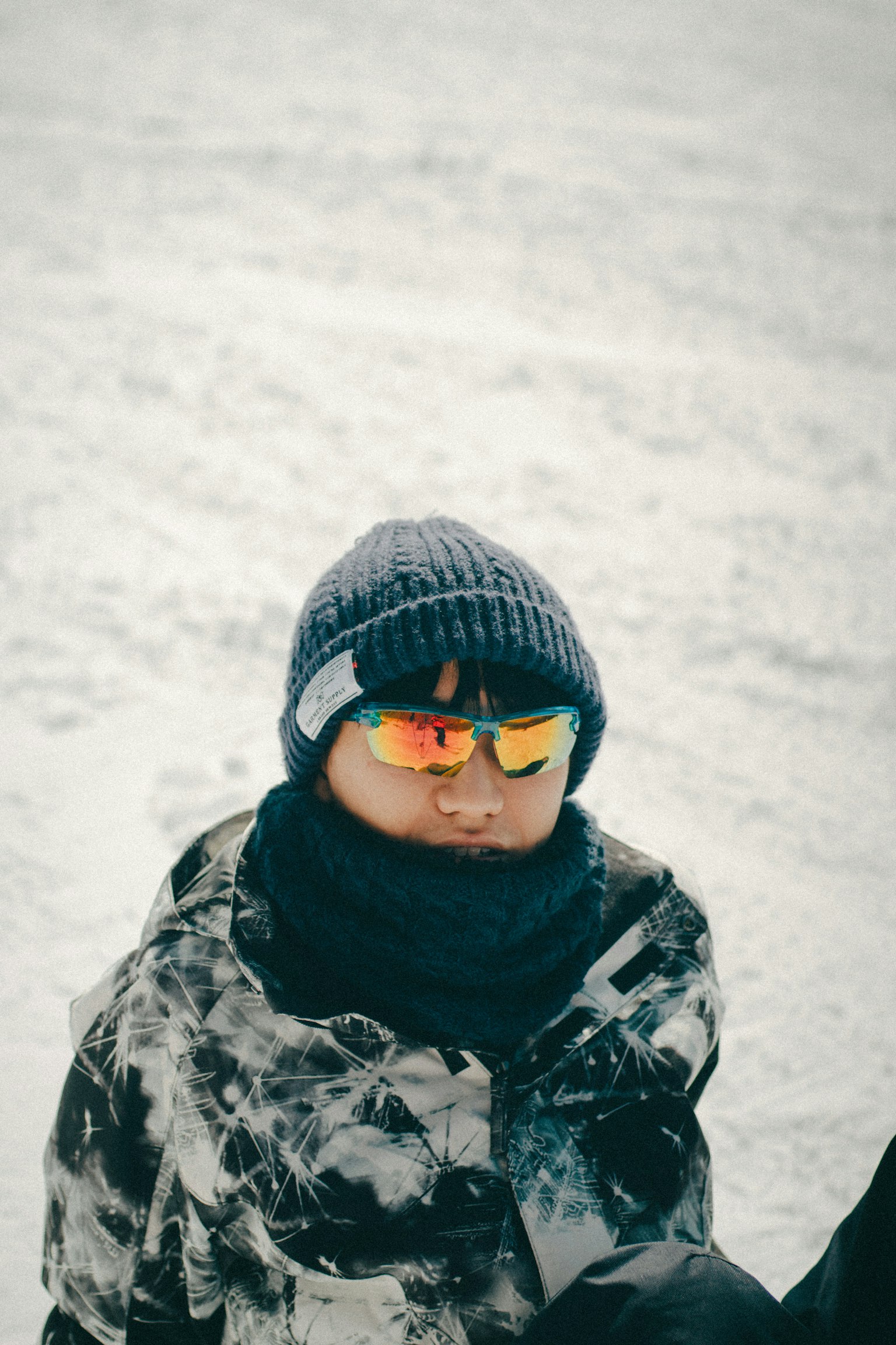 一个坐在雪地里的男孩戴着针织帽和太阳镜