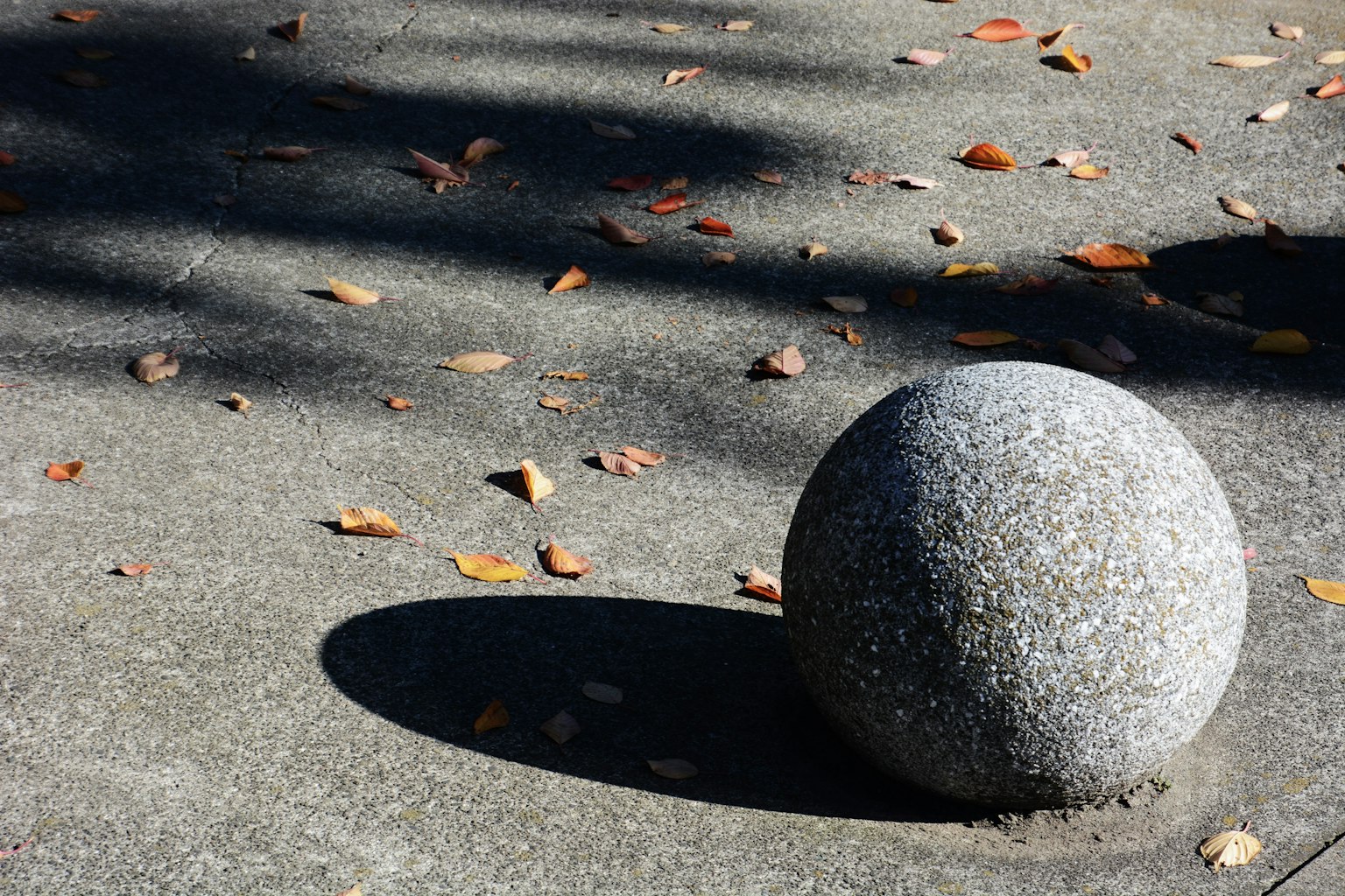 A round stone sculpture on a concrete surface with fallen leaves