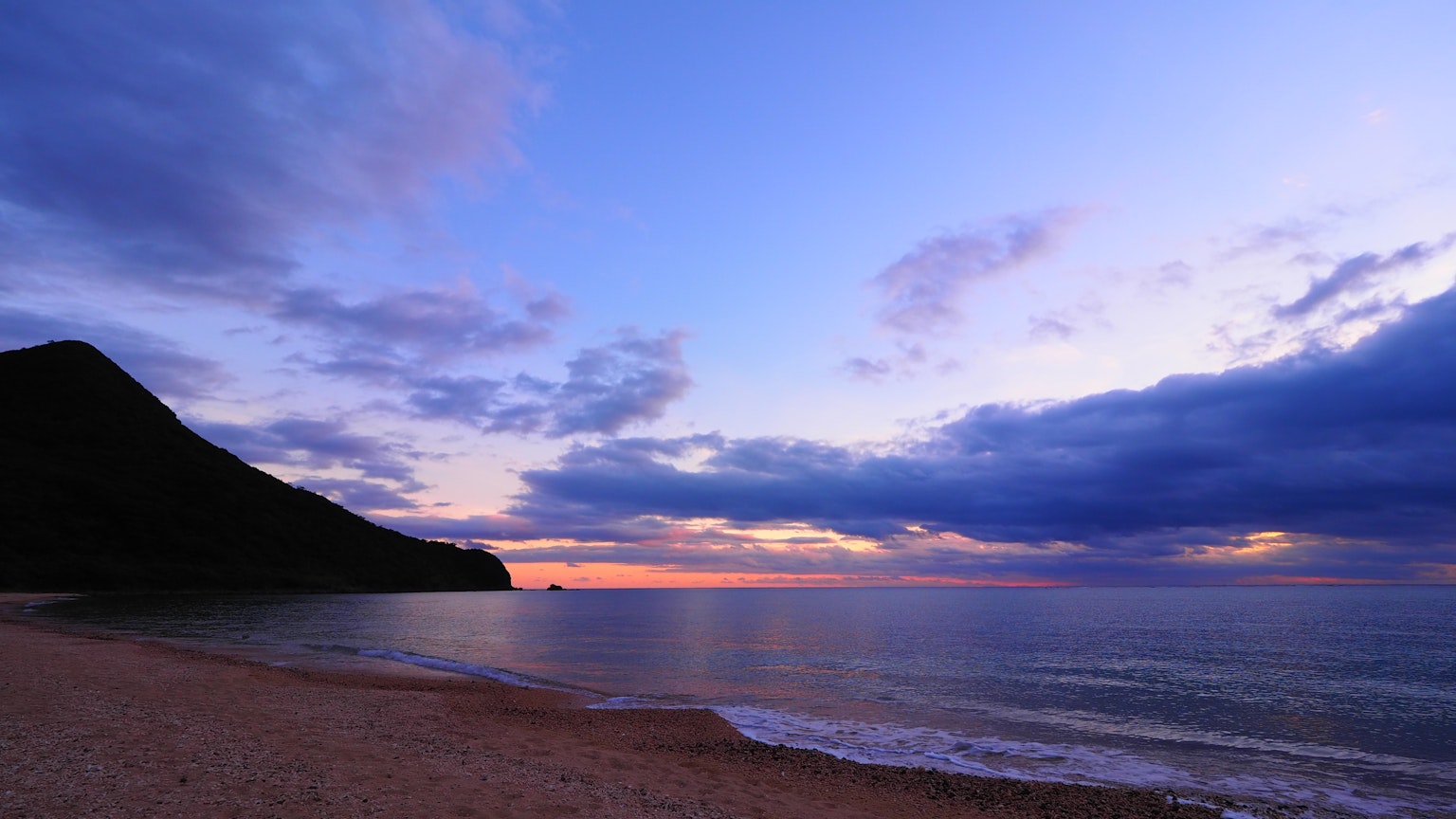 Twilight beach scene with silhouette of mountain and calm sea