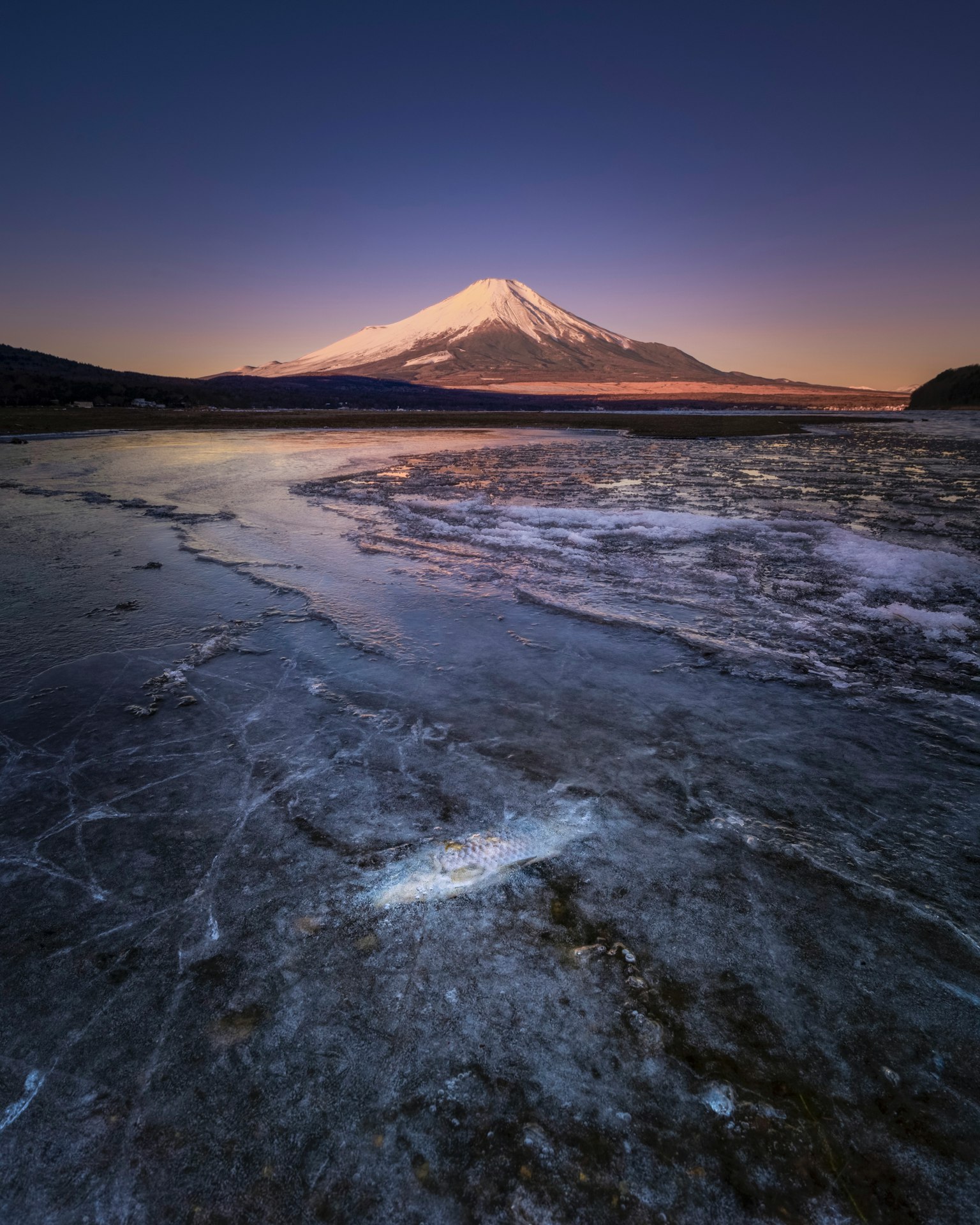 Beautiful Mount Fuji covered in snow near a tranquil lake illuminated by twilight