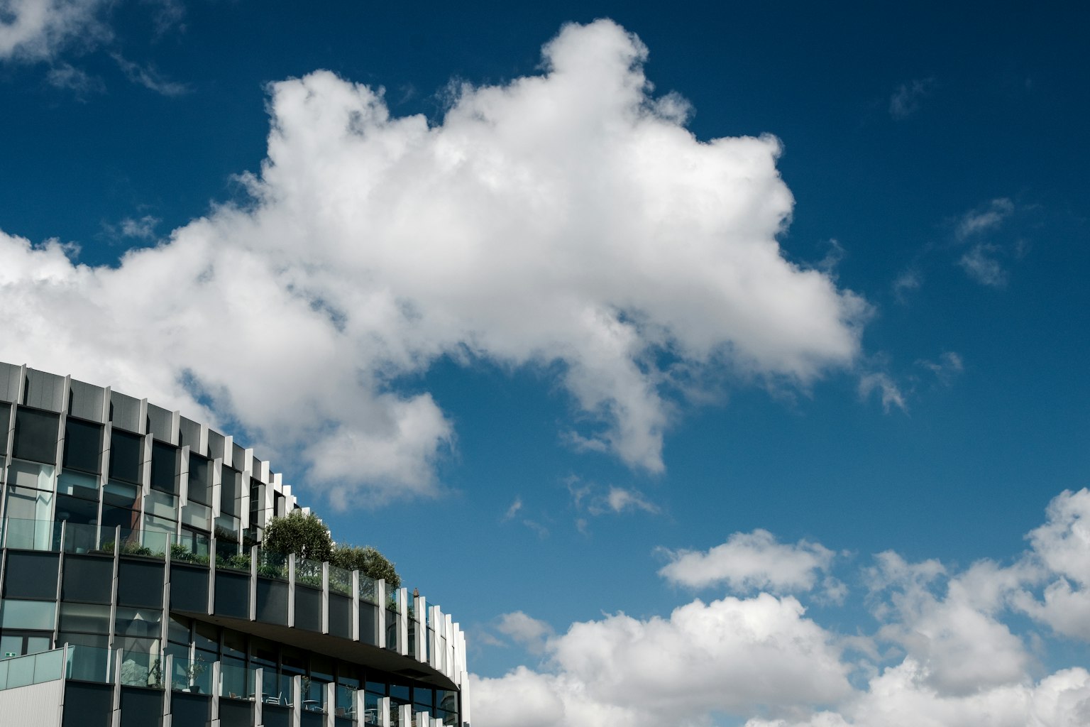Un edificio moderno parzialmente visibile sotto un cielo blu con nuvole bianche e soffici