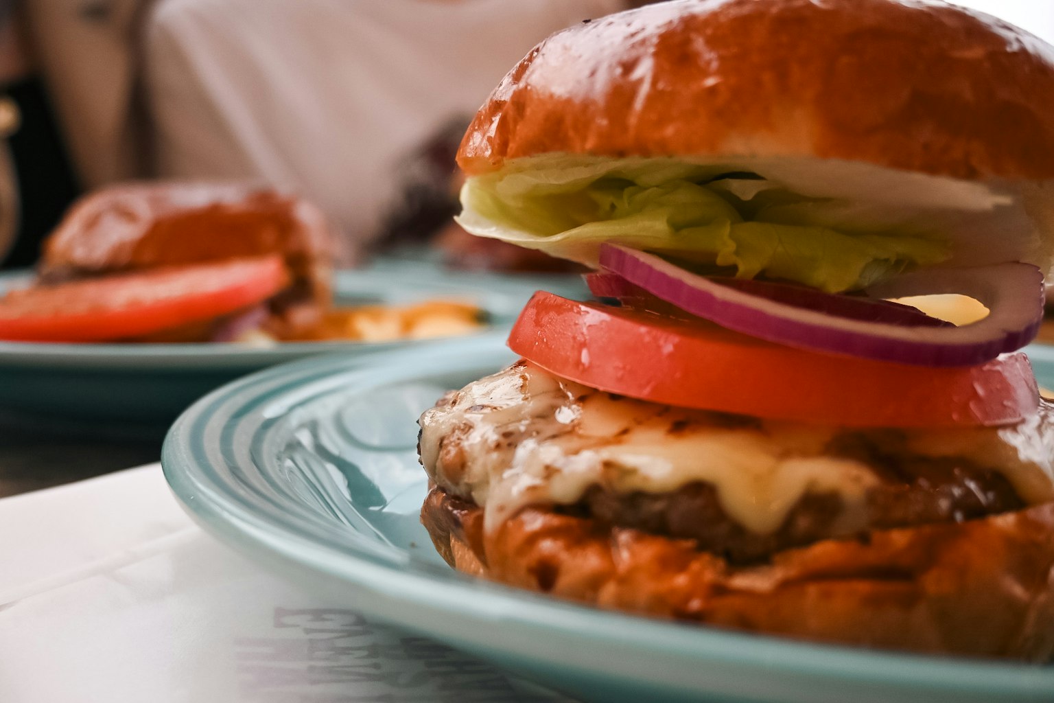 Bánh hamburger ngon được phục vụ trên đĩa màu xanh Bánh mềm có xà lách cà chua và hành tây