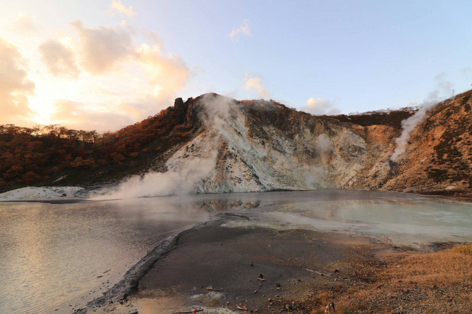 Pemandangan vulkanik dengan sumber air panas diterangi oleh matahari terbenam