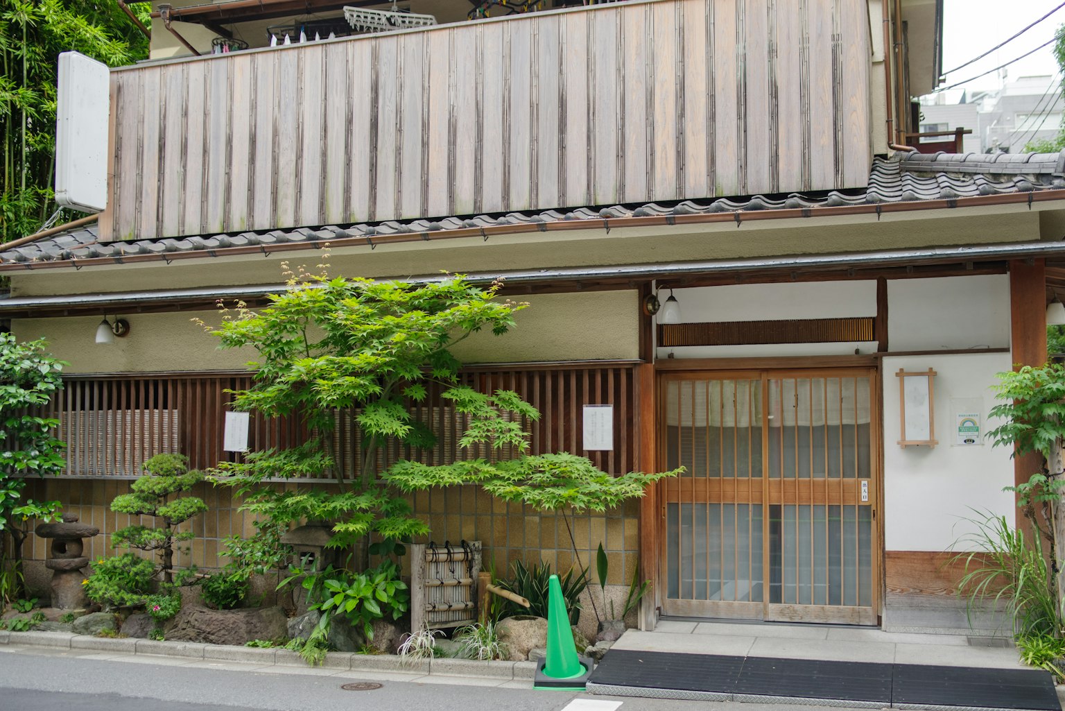 传统日本木屋外观，周围有绿色植物和木门