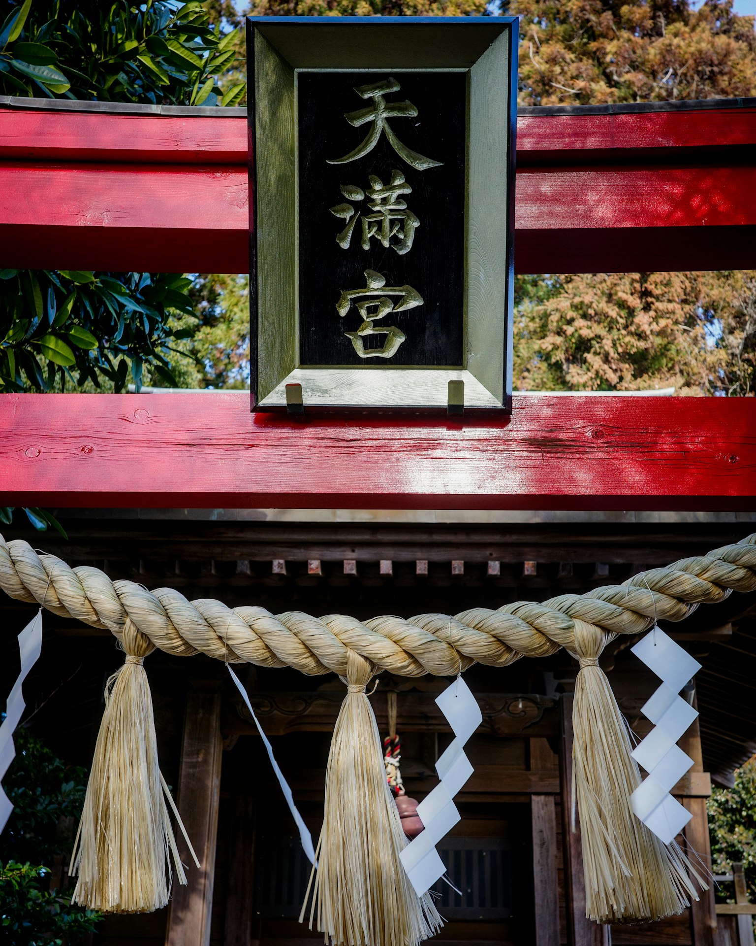 Cổng torii đỏ rực với biển báo ghi Khu đền Tenmangu được trang trí bằng shide truyền thống